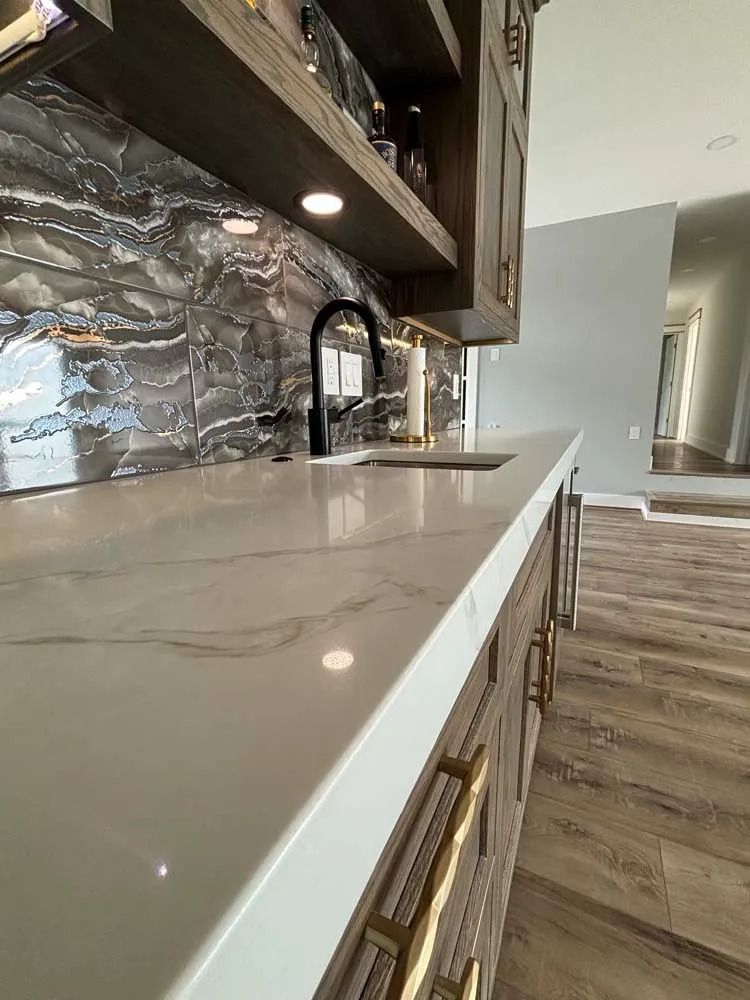 Modern kitchen countertop with marble backsplash, black faucet, and wood flooring along a bright hallway