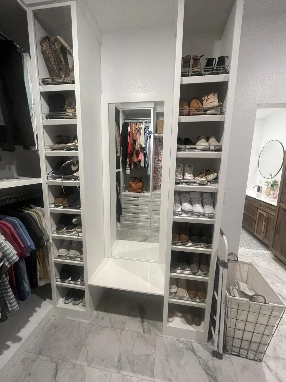 Walk-in closet with shelves, hanging clothes, a central mirror, and a white storage basket on the floor