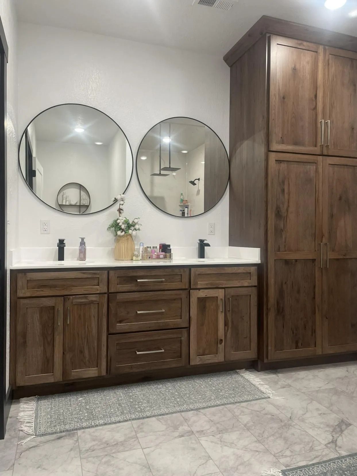 Modern bathroom vanity with dark wood cabinets, two round mirrors, and a tall matching storage cabinet.
