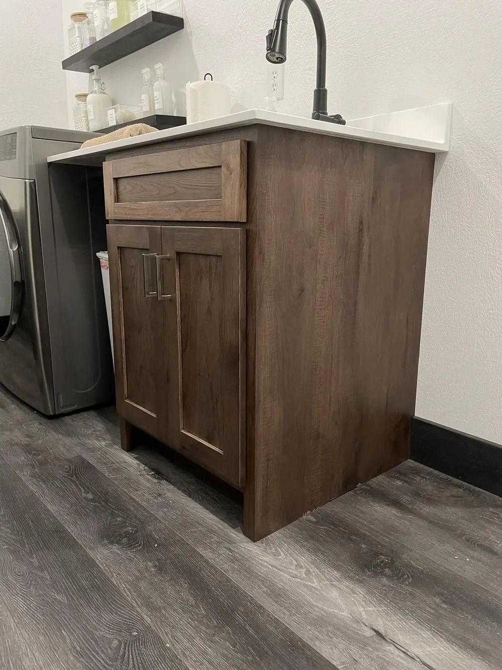 Small kitchen sink cabinet with dark wood finish, black faucet, and a mini fridge beside it in a room corner Small kitchen sink cabinet with dark wood finish, black faucet, and a mini fridge beside it in a room corner