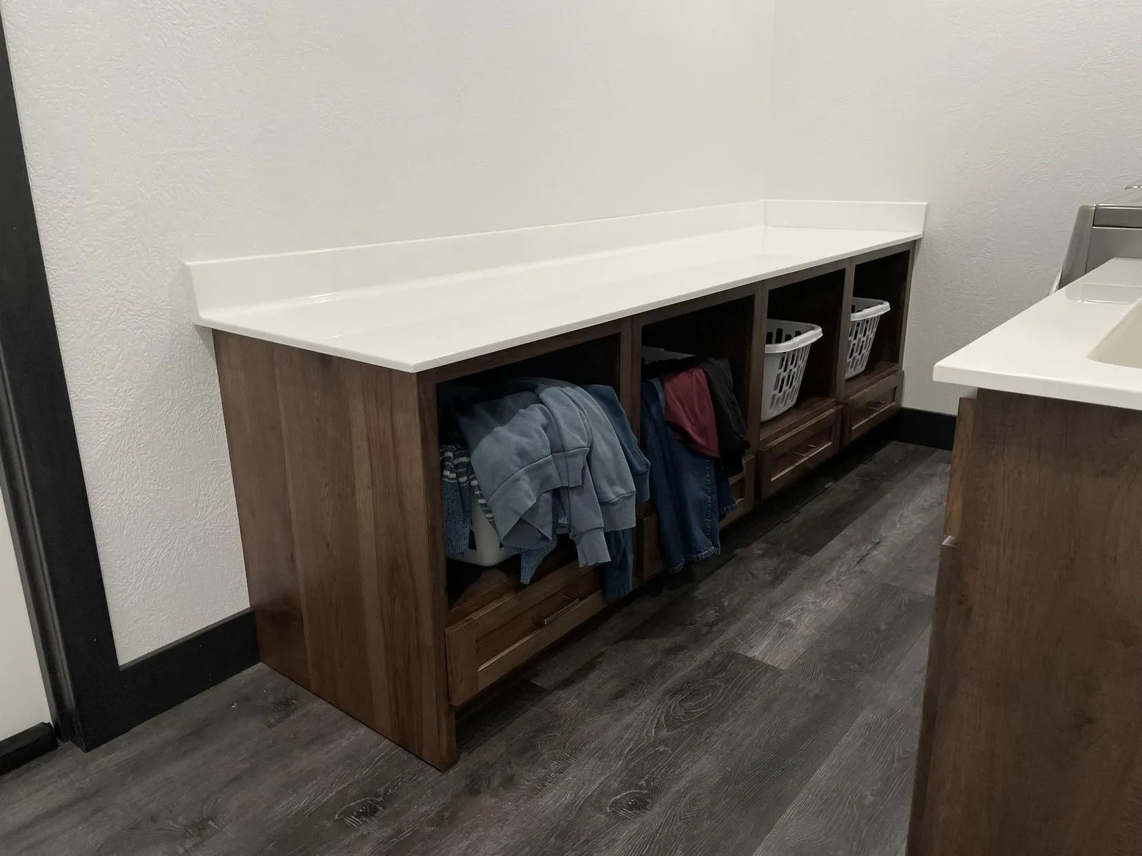 Wooden storage bench with white top, cubbies, hanging jackets, and a basket in a hallway.