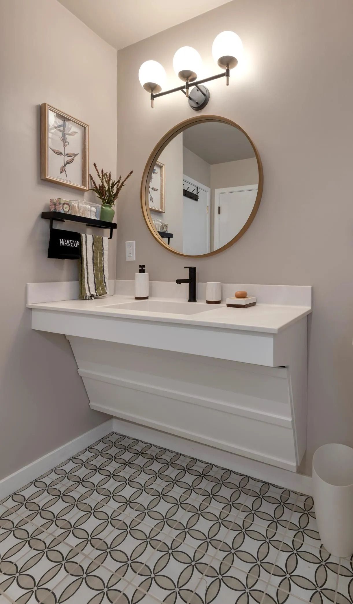 Small modern bathroom vanity with round mirror, wall light, and patterned tile floor.