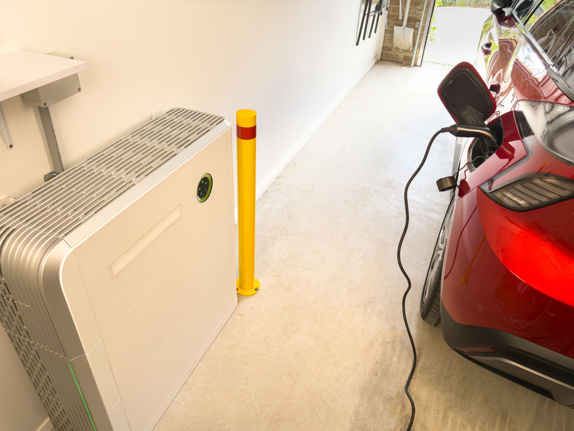 Yellow bollard in a parking garage beside a white radiator and a red car charging cable. Yellow bollard in a parking garage beside a white radiator and a red car charging cable.