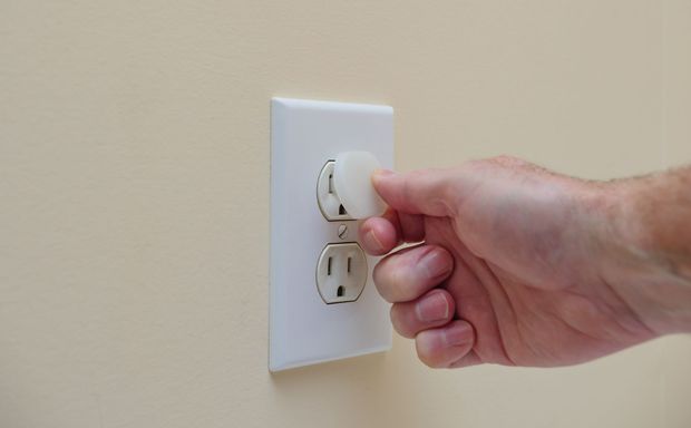Hand turning a plug in a white wall outlet on a beige wall Hand turning a plug in a white wall outlet on a beige wall