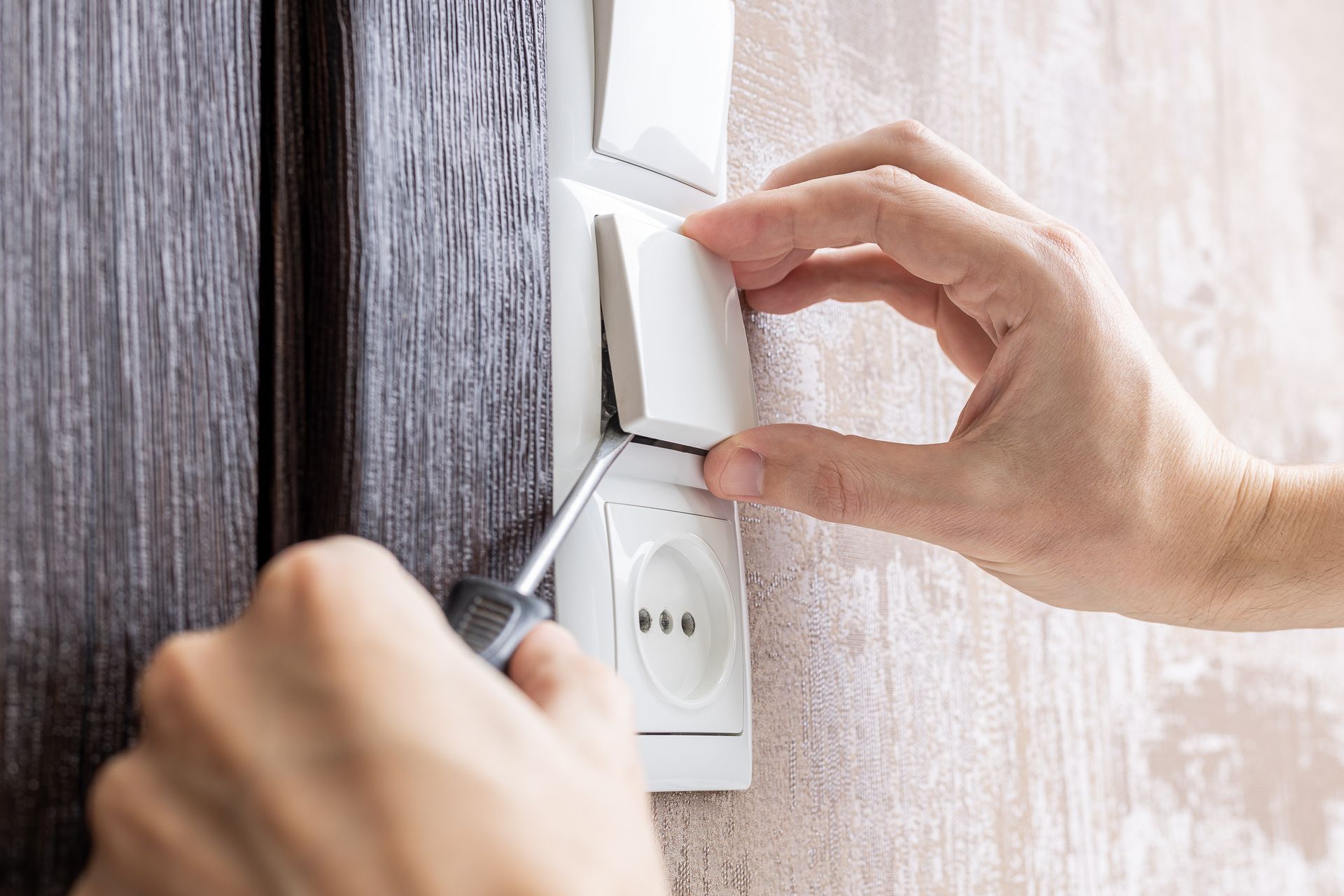 Hands mounting a white light switch beside a wall outlet with a screwdriver Hands mounting a white light switch beside a wall outlet with a screwdriver