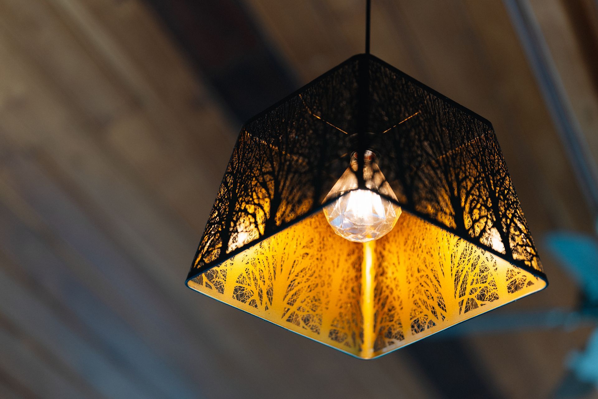Black geometric pendant lamp with warm yellow light against a wooden ceiling