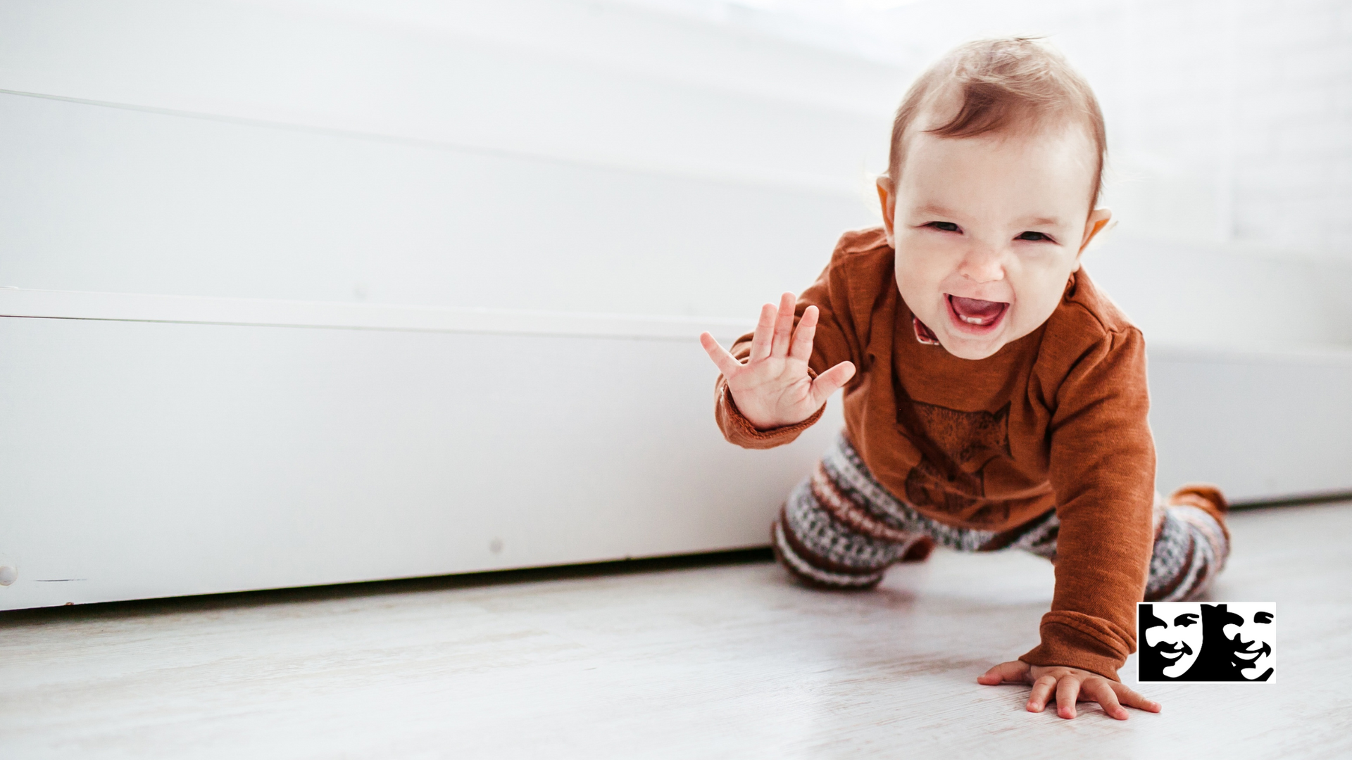 A baby is crawling on the floor and smiling.