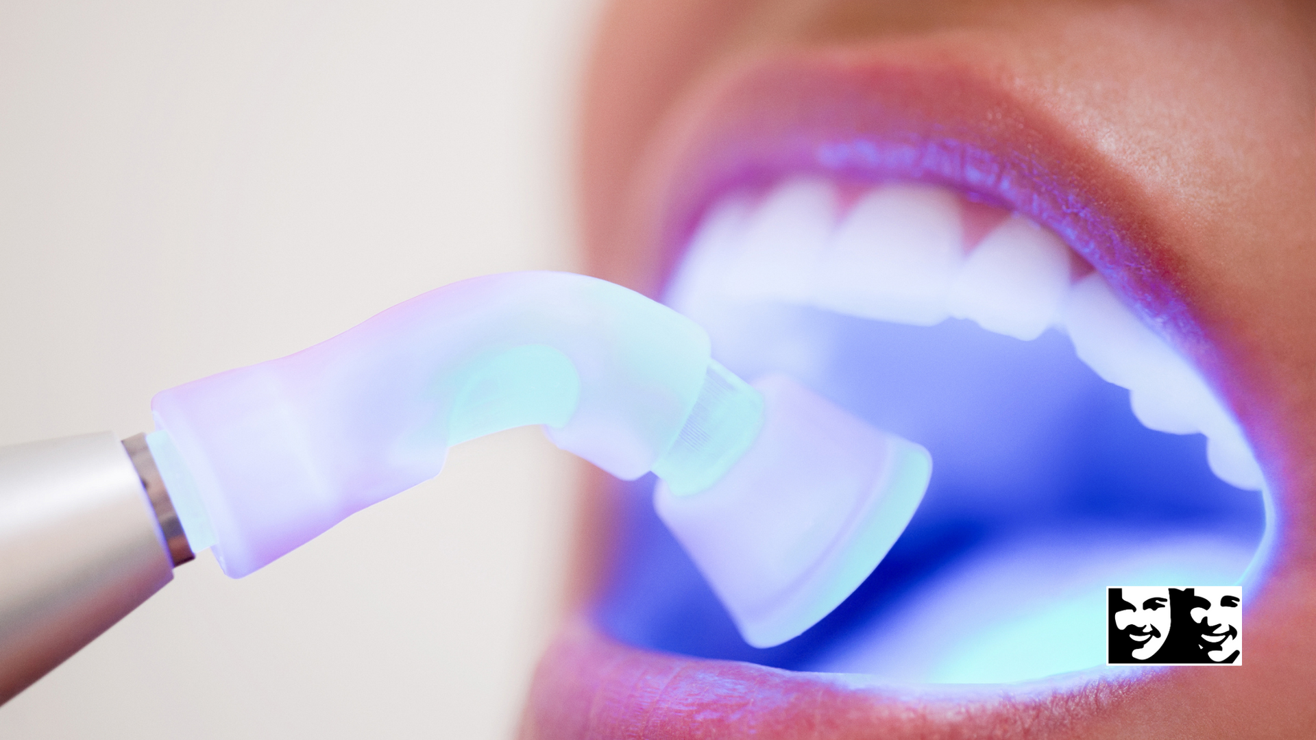 A woman is getting her teeth whitened with a blue light.