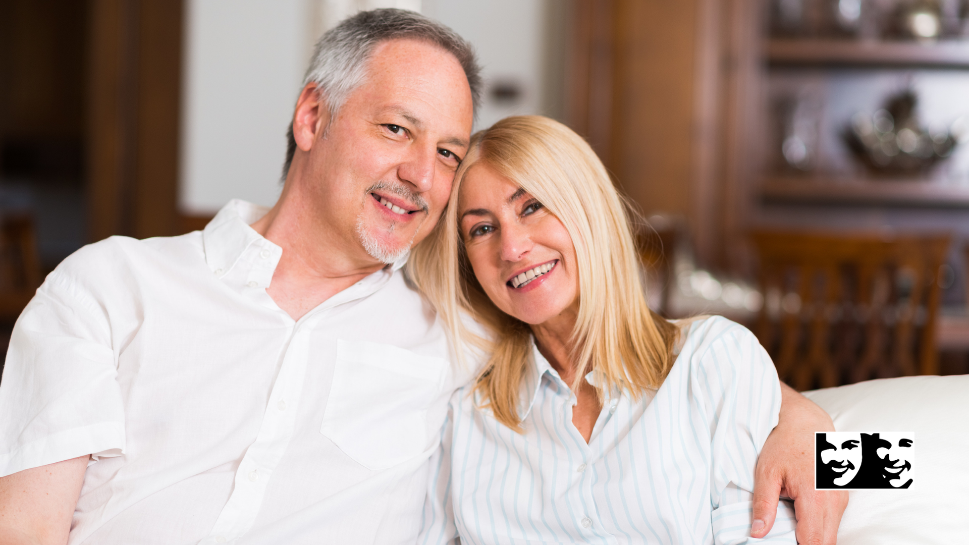 A man and a woman are sitting on a couch and smiling for the camera.