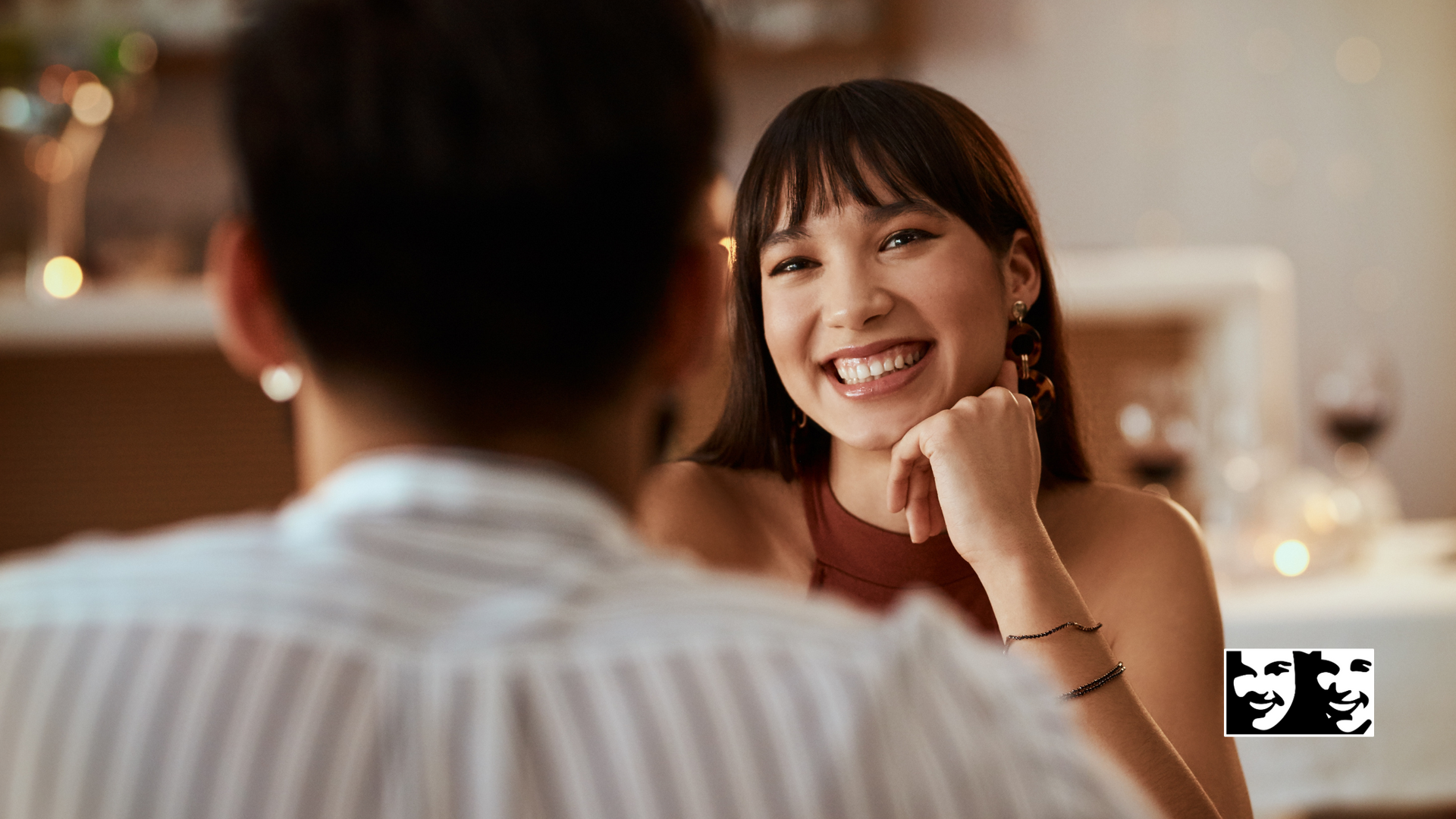 A man and a woman are sitting at a table looking at each other and smiling.