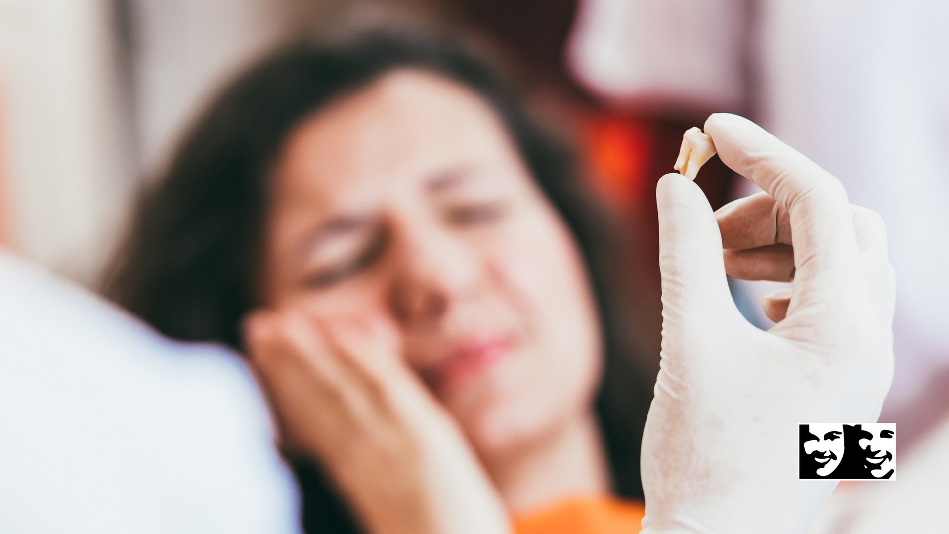 A dentist holding an extracted tooth in front of a woman in discomfort, inside a dental office.