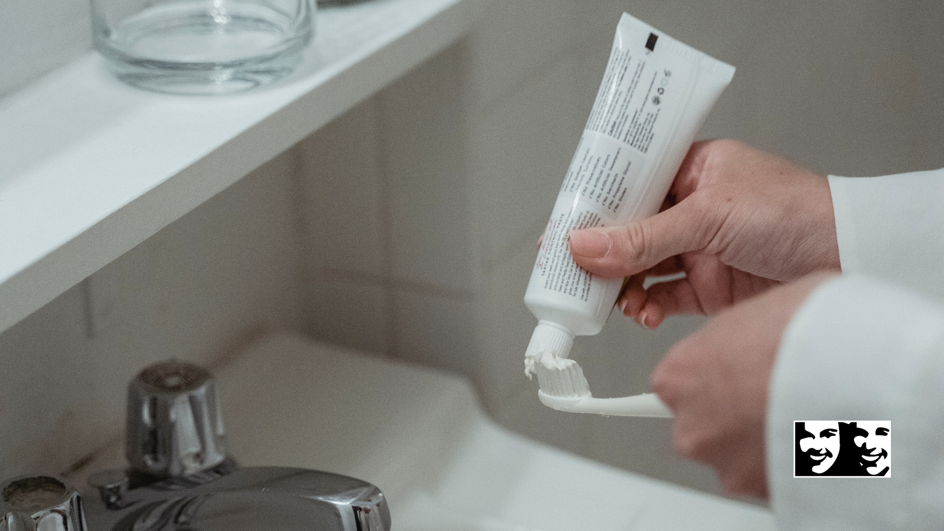 Person squeezing toothpaste onto a toothbrush in a bathroom.