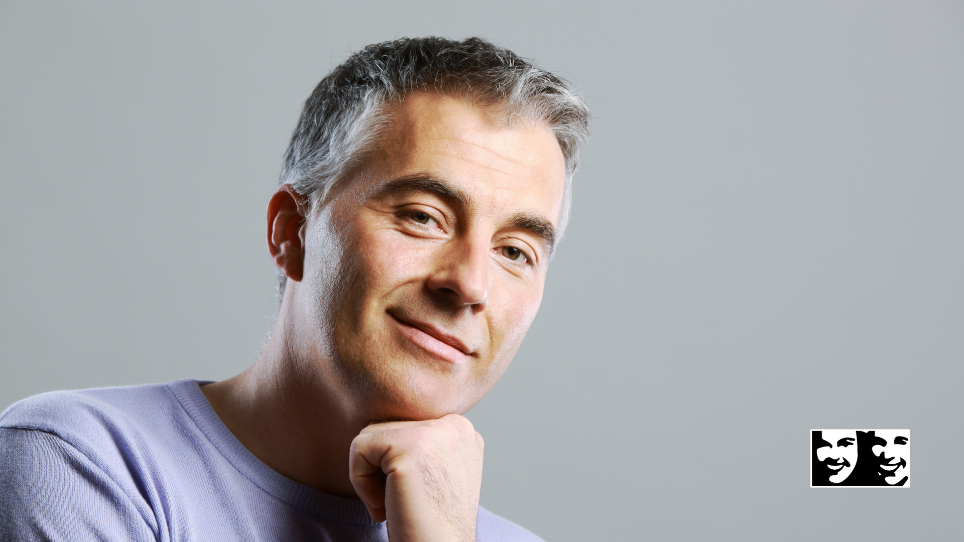 A man with gray hair is smiling with his hand on his chin.
