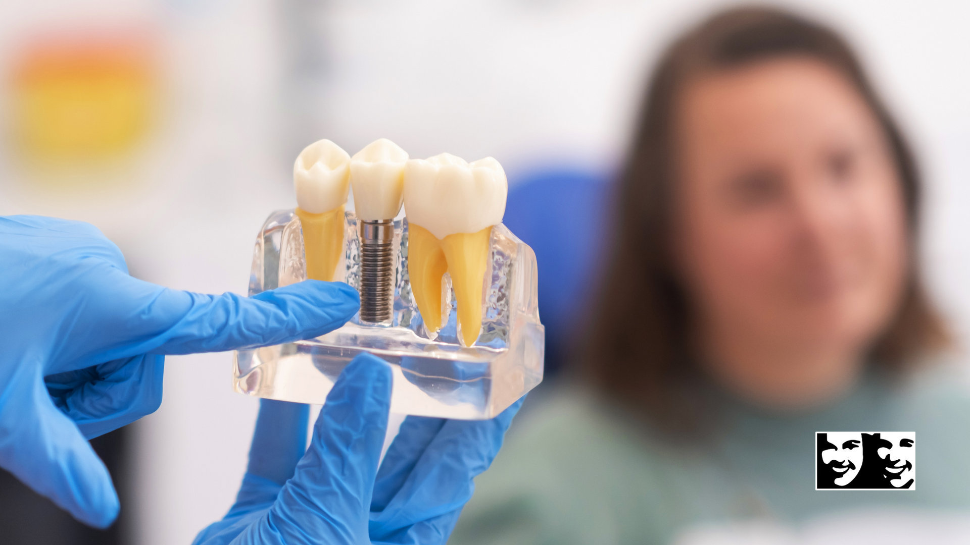 A dentist is holding a model of dental implants in front of a woman.