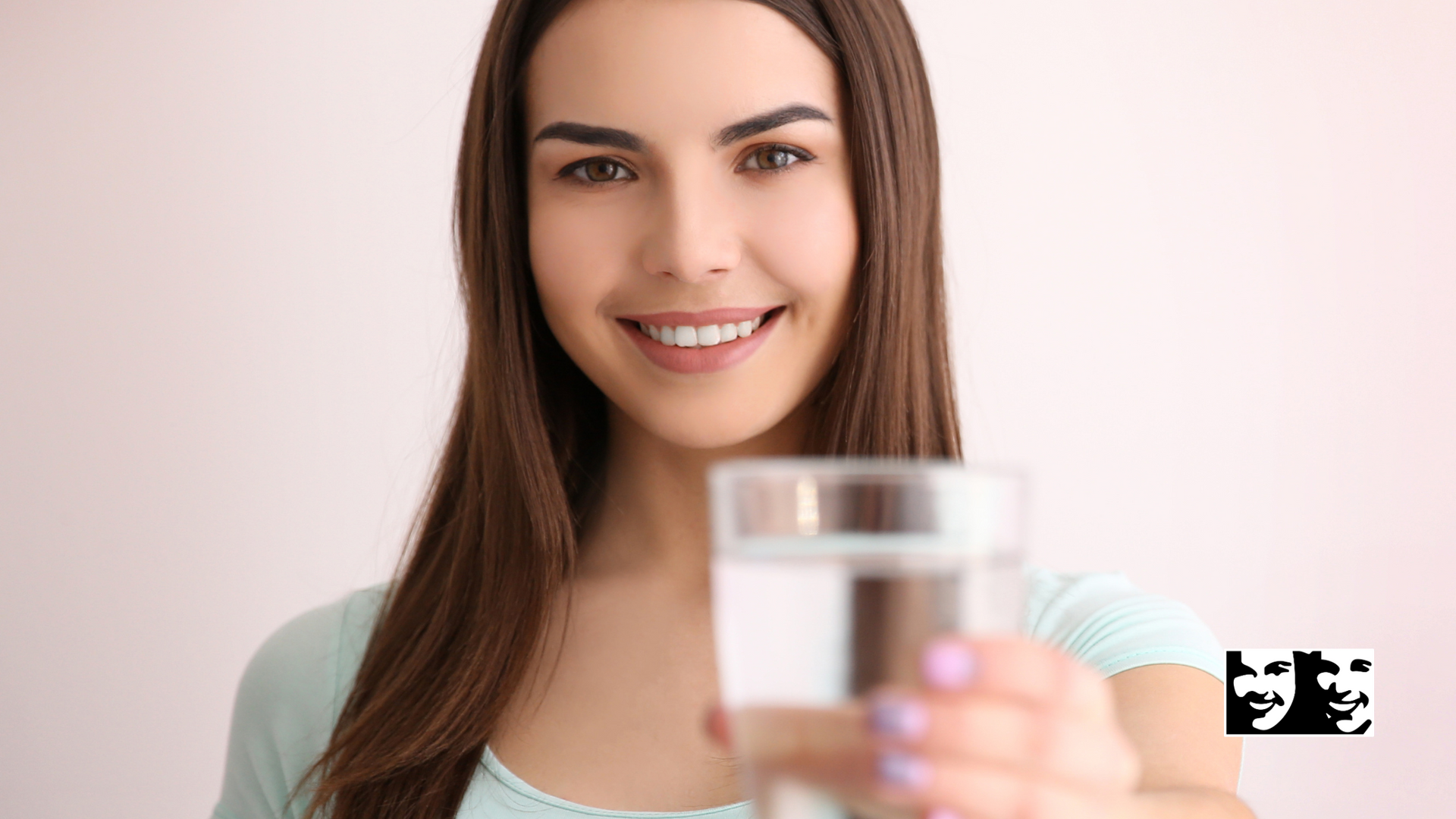Woman smiling, holding out a glass of water, light background.