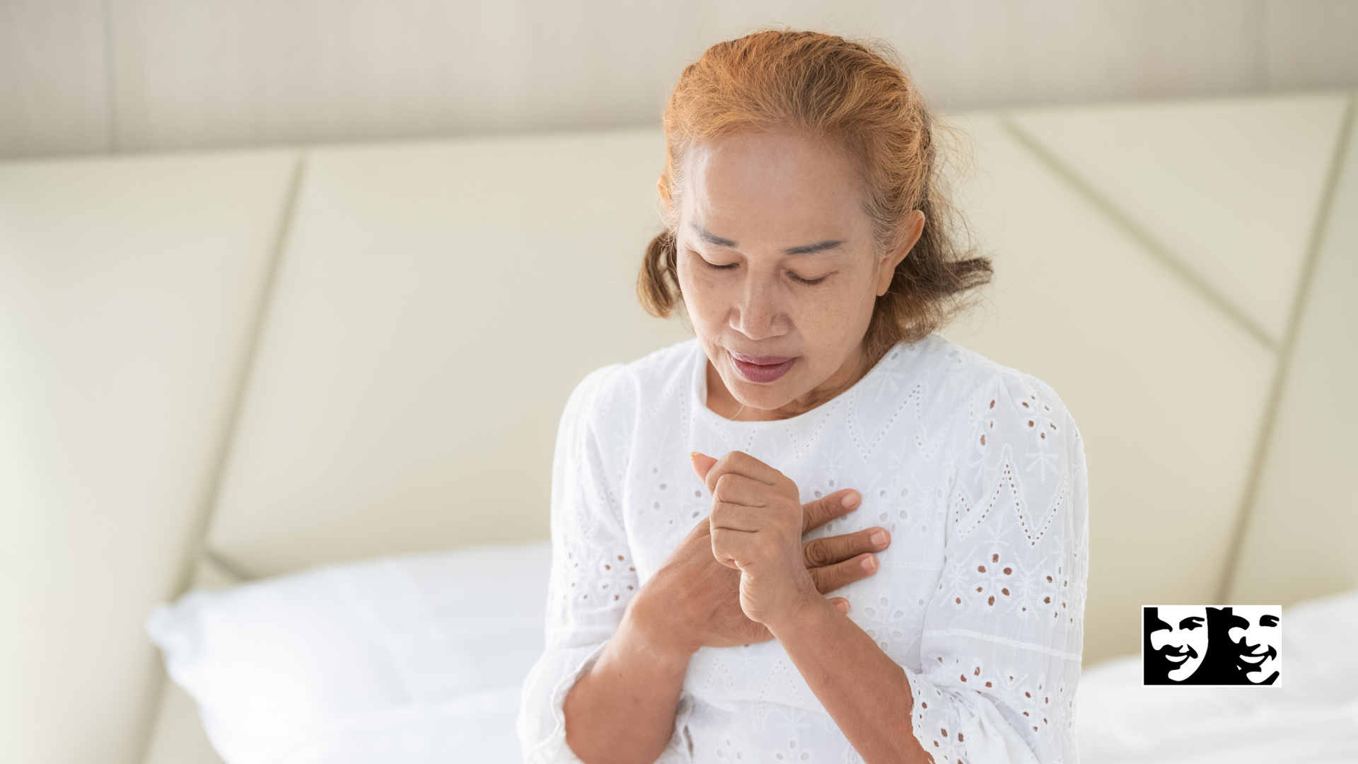 A woman is sitting on a bed with her hands on her chest.
