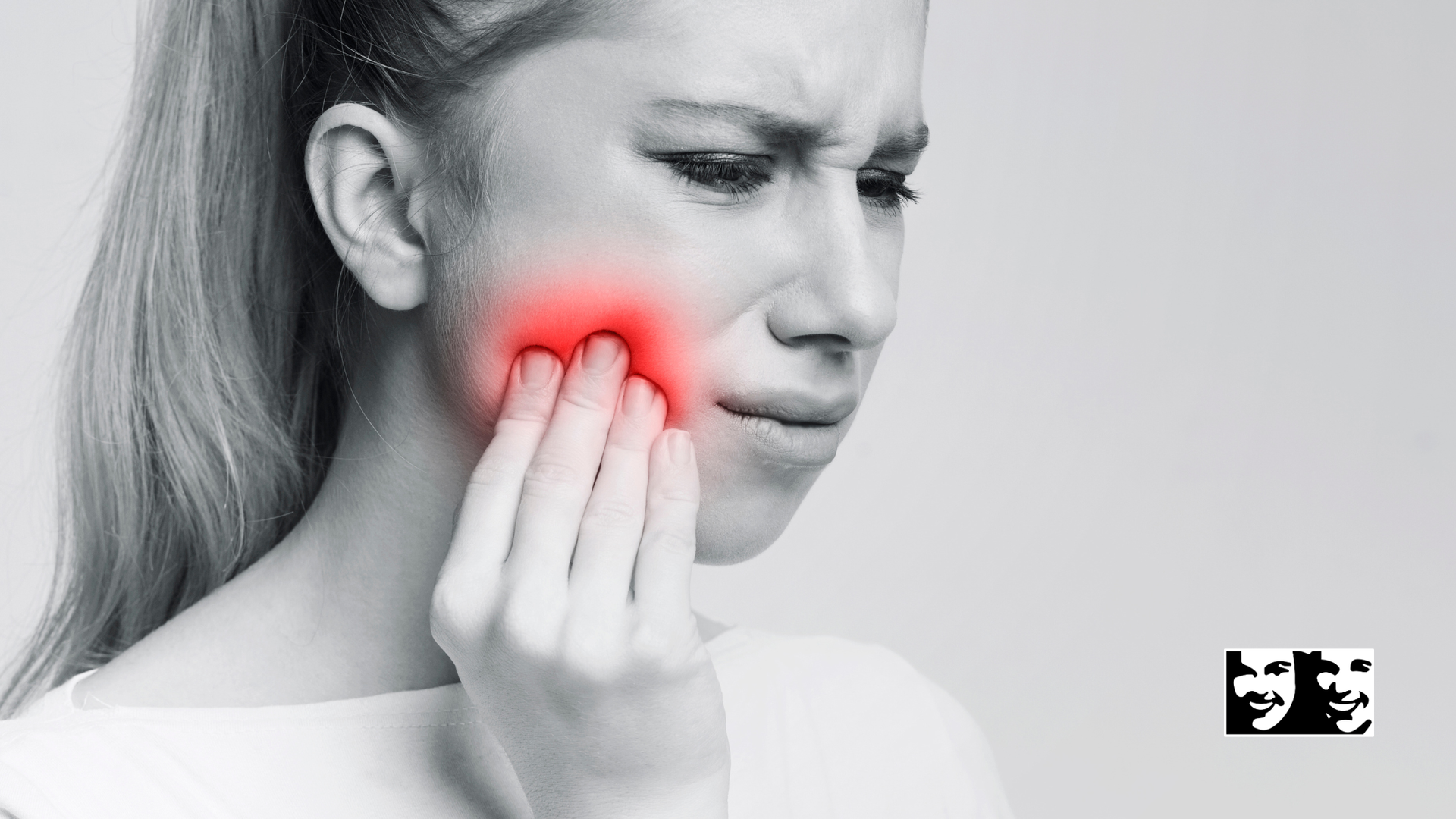 Person holding a glowing red cheek, grimacing in pain on a grayscale background