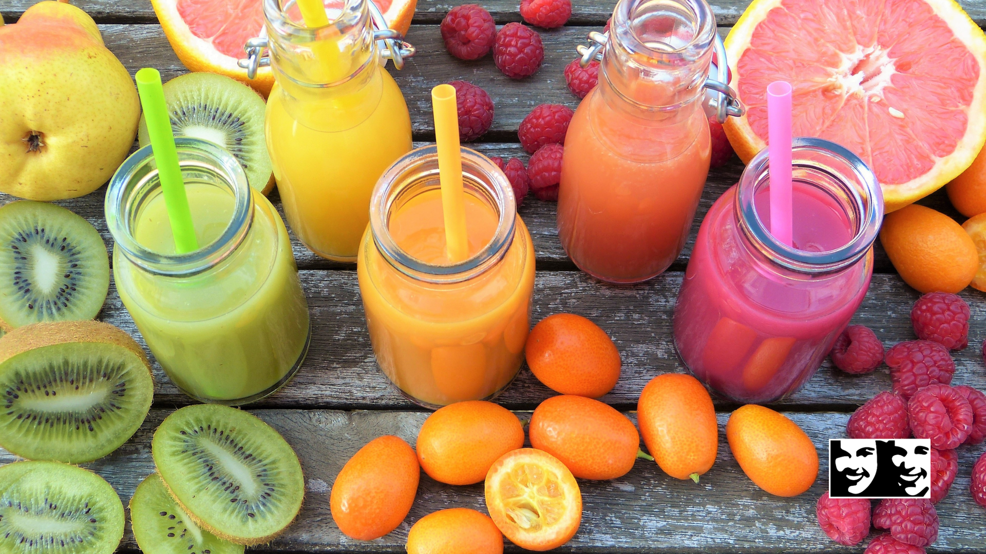 Colorful fruit smoothies in glass jars with straws, surrounded by fresh fruit.