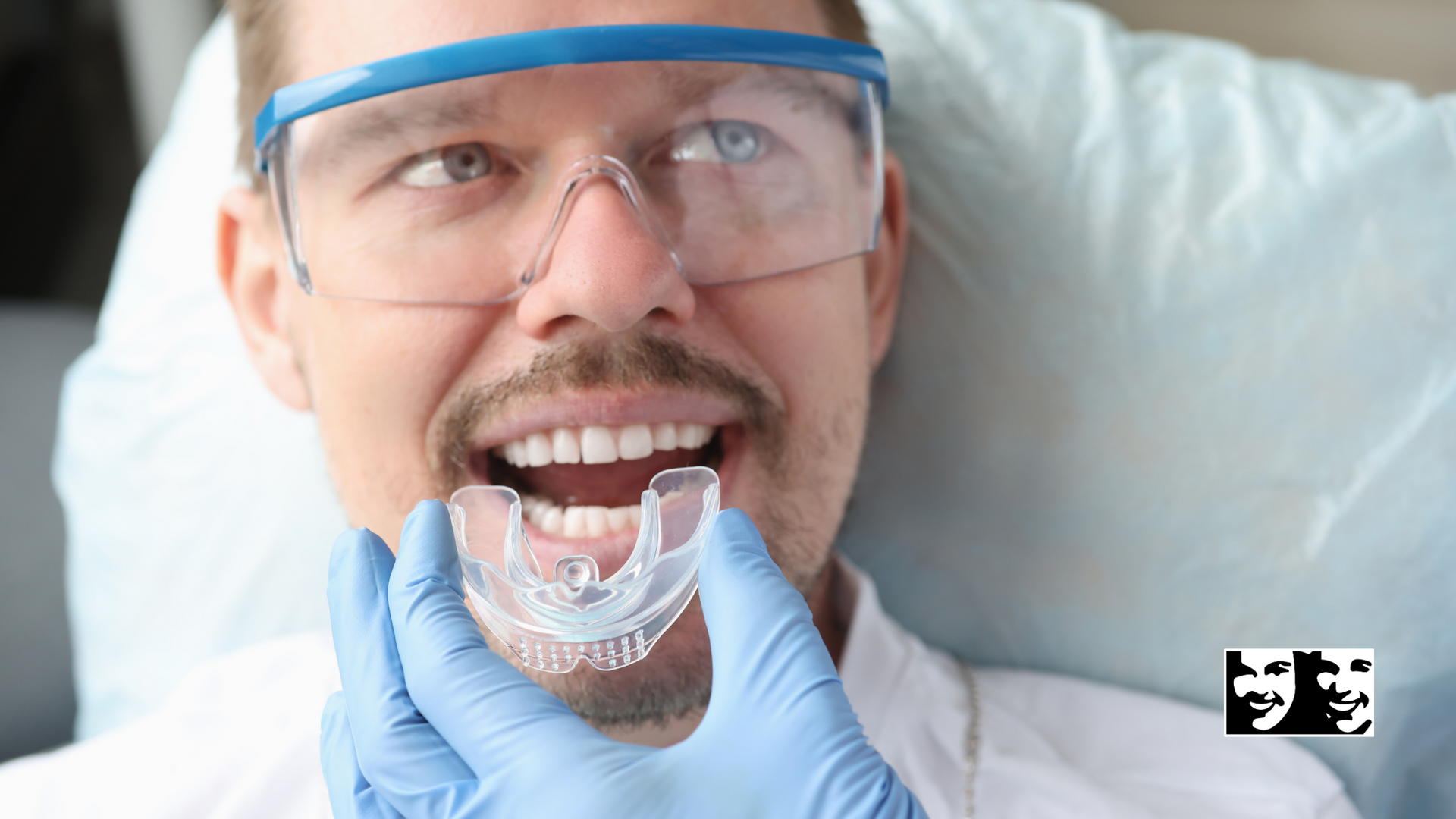 A man wearing glasses and gloves is holding a mouth guard in his mouth.