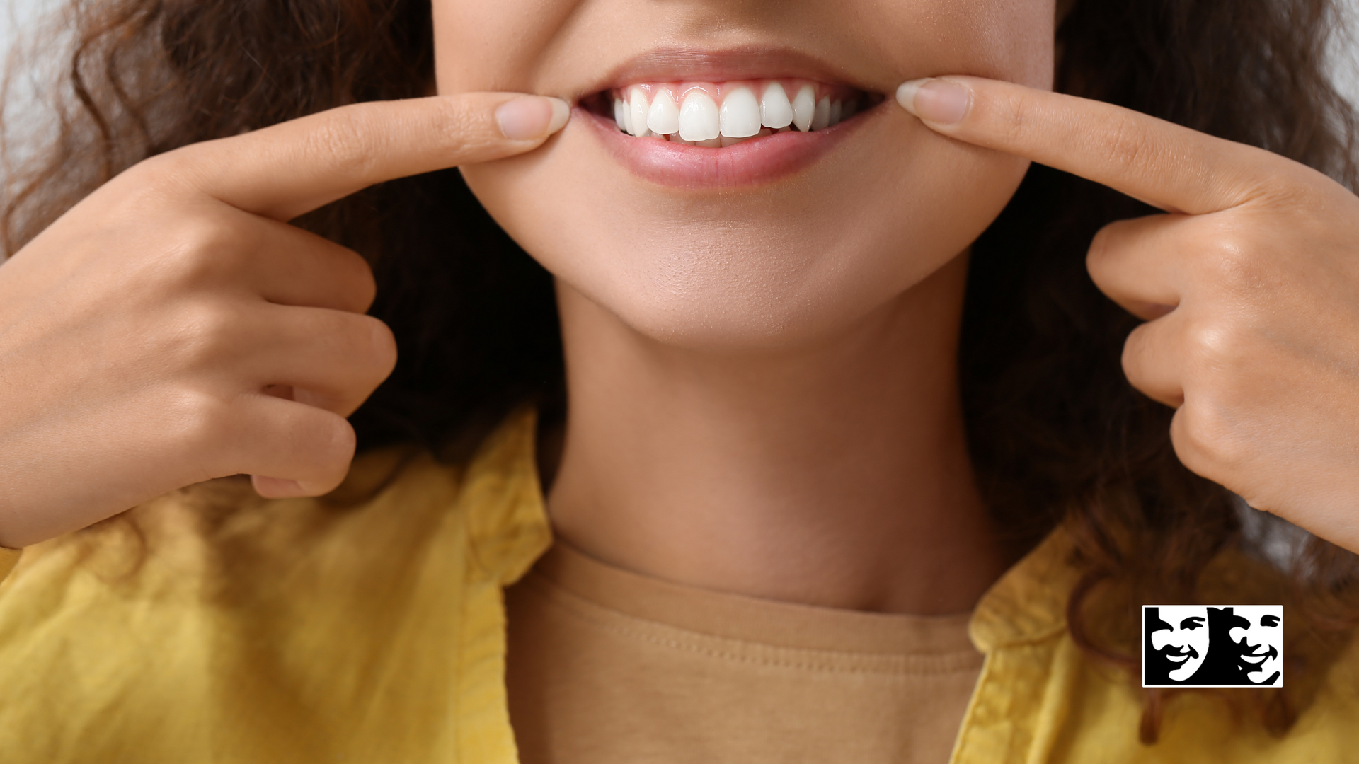 A woman is pointing at her teeth with her fingers.