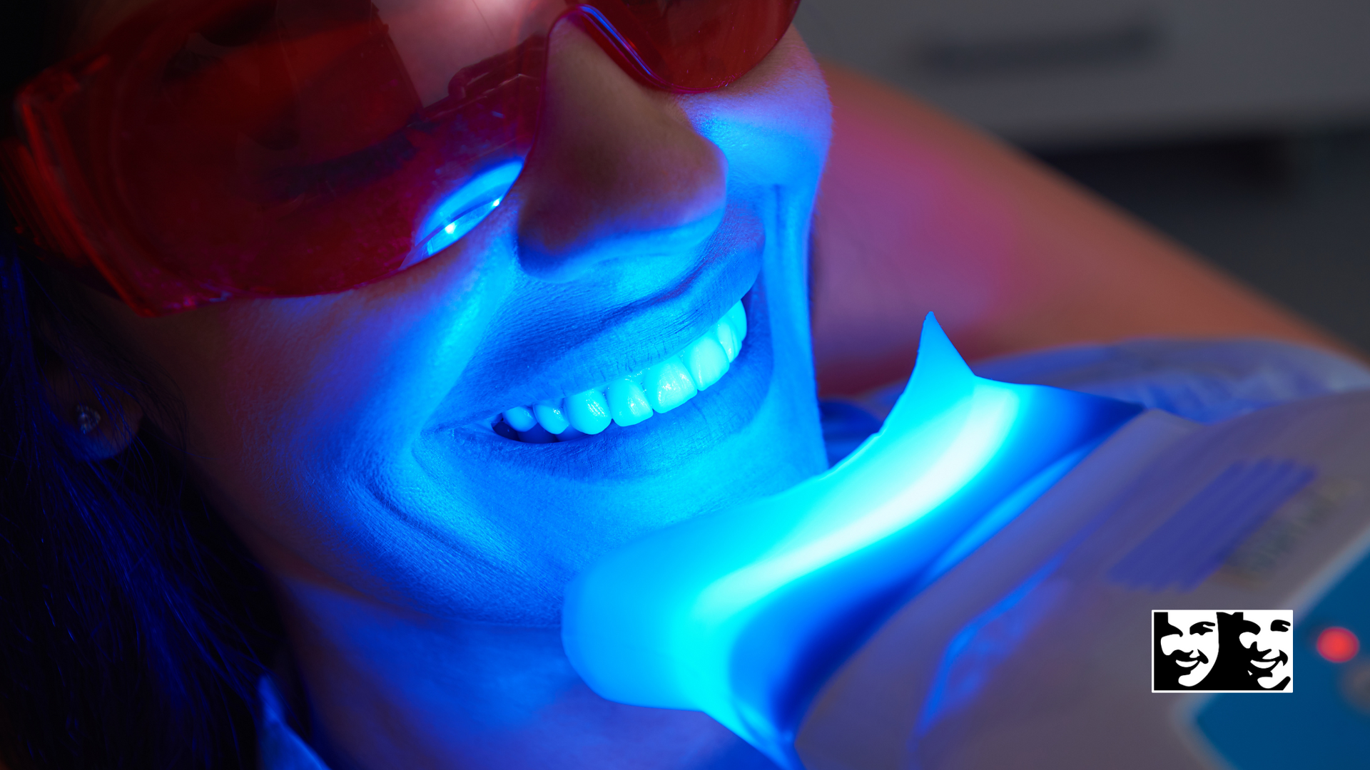 A woman is getting her teeth whitened with a blue light.