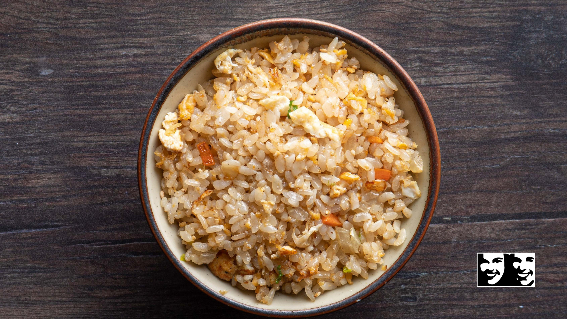 Bowl of fried rice on a dark wooden surface; visible ingredients include rice, egg, and vegetables.