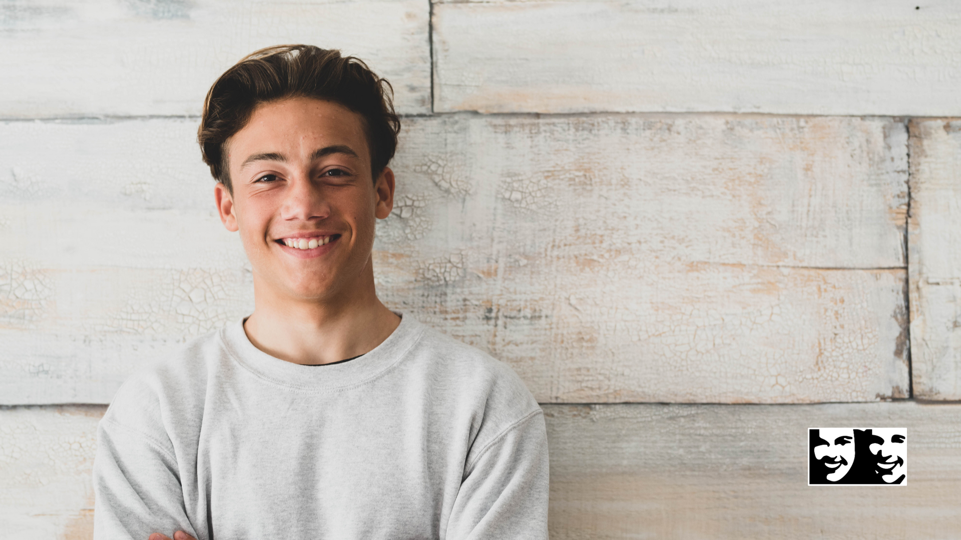 A young man is smiling while standing in front of a wooden wall.