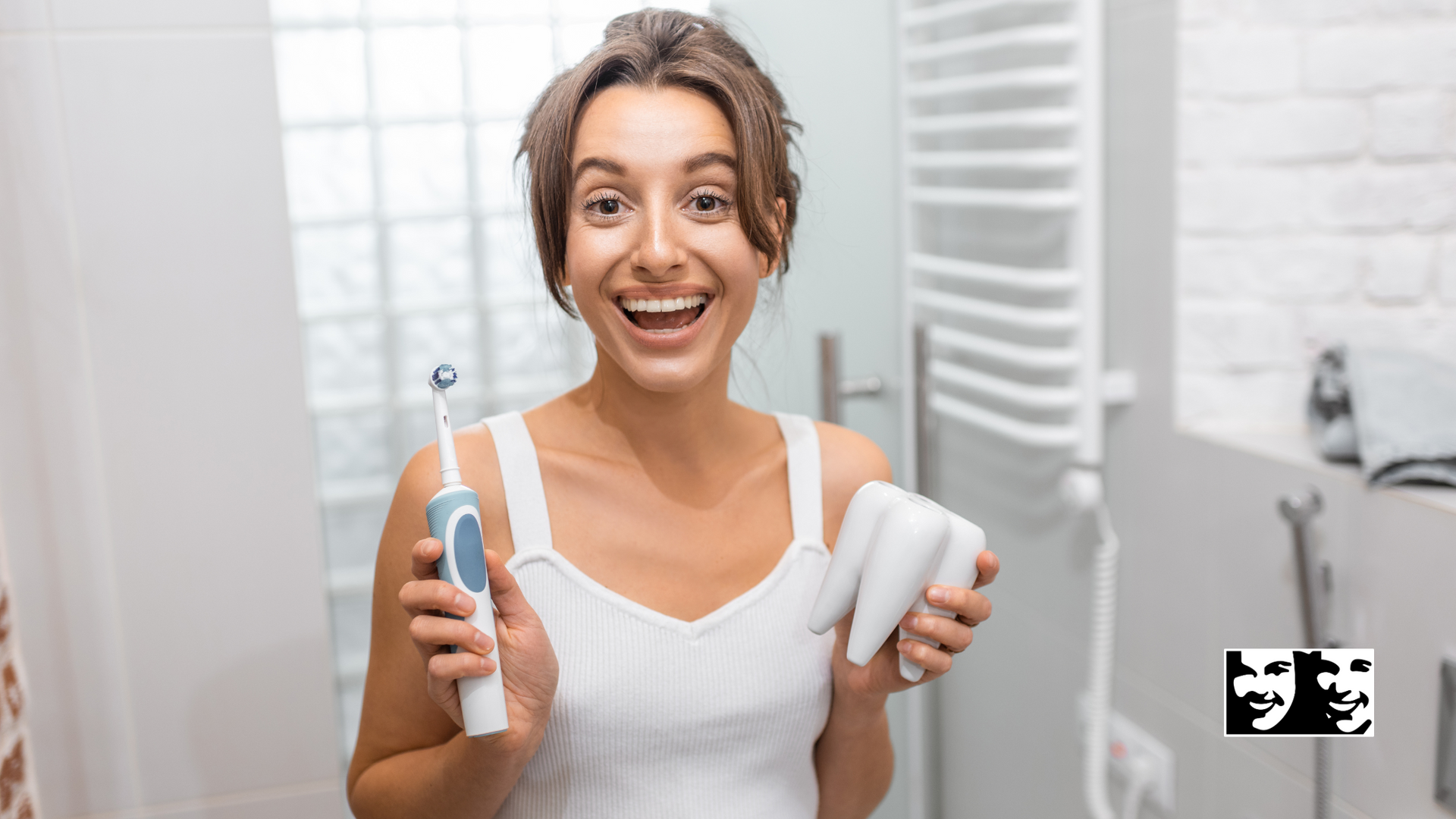 A woman is holding an electric toothbrush and a tube of toothpaste in a bathroom.