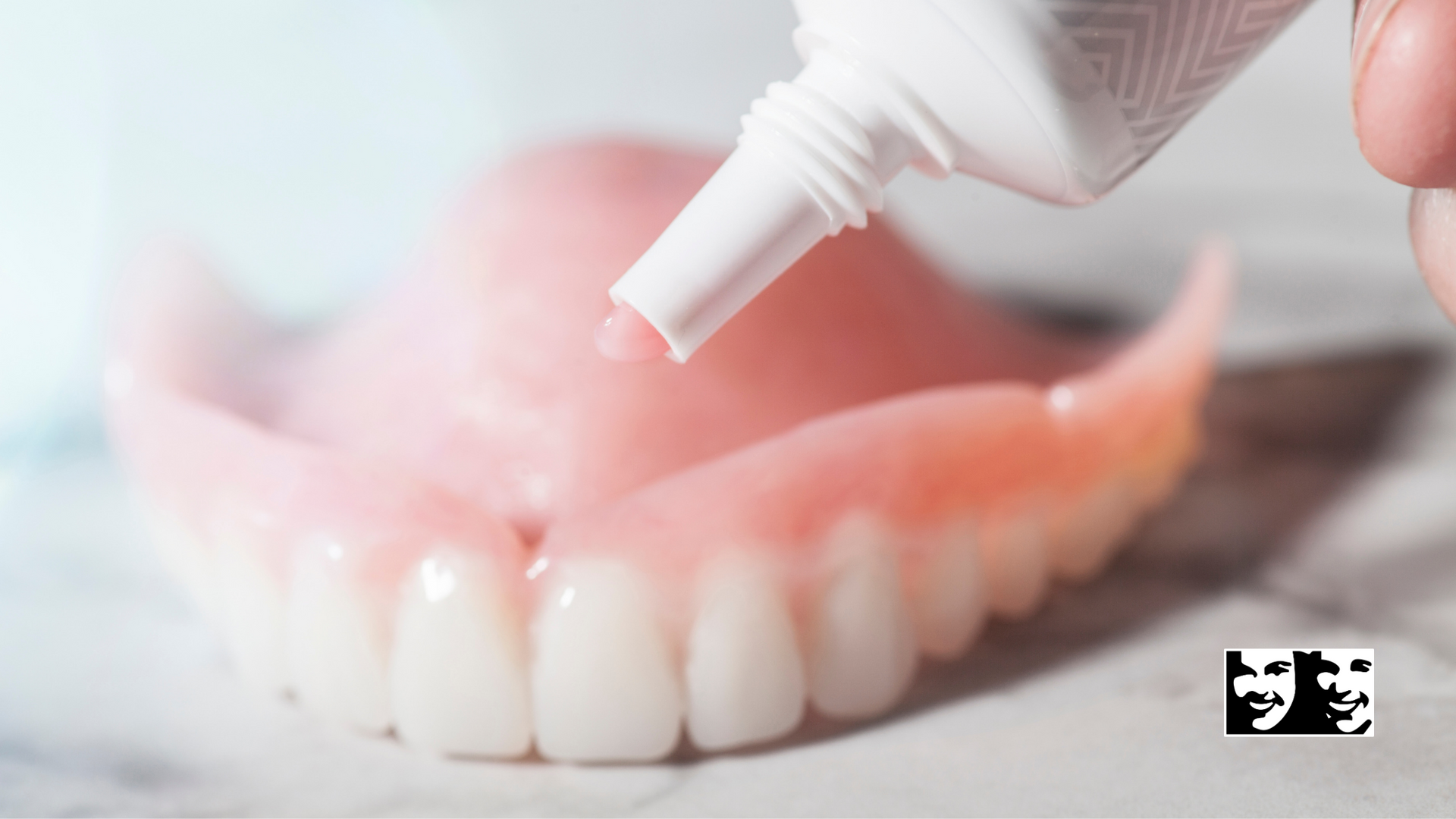 A person is applying toothpaste to a denture.