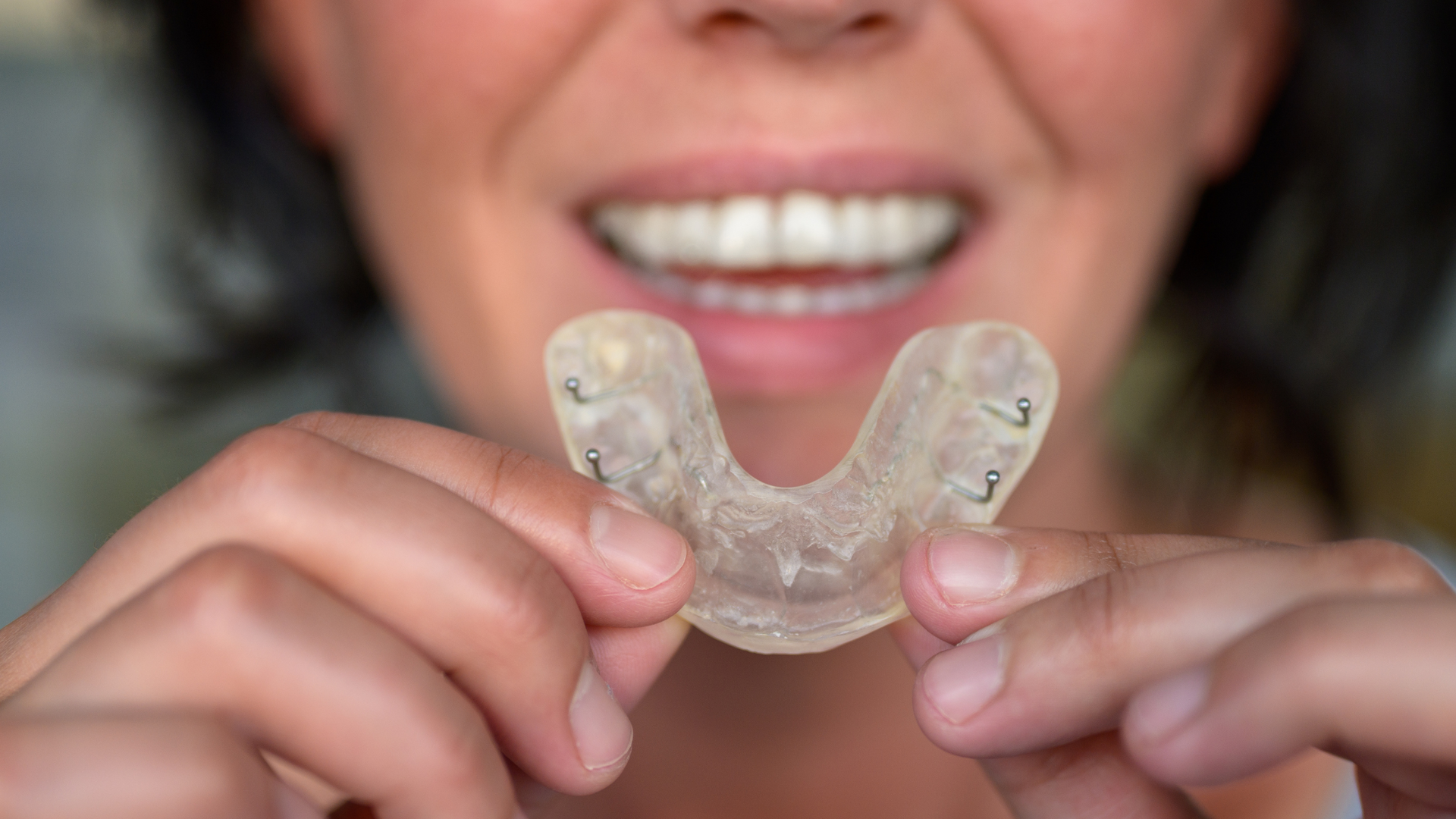 A woman is holding a clear mouth guard in front of her mouth.