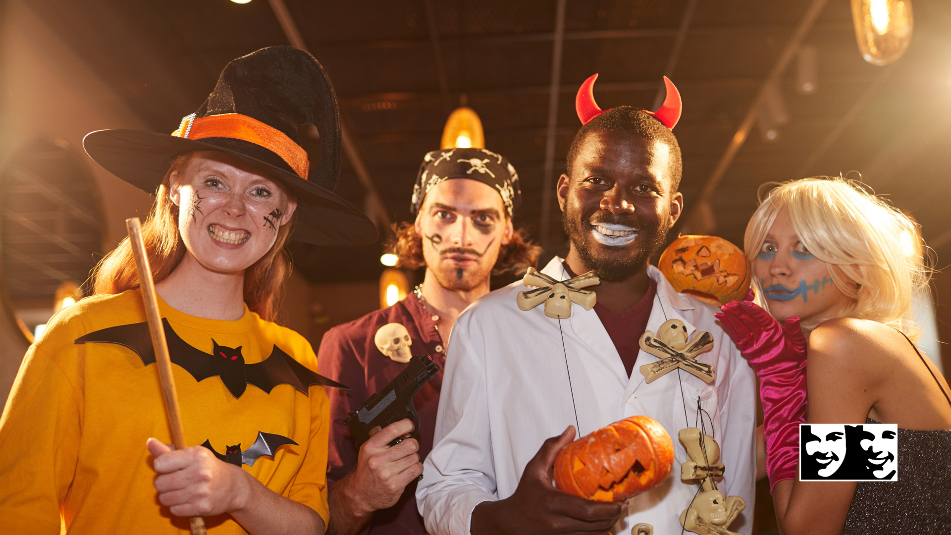 Four people in Halloween costumes smile indoors; witch, devil, vampire, and ghost.