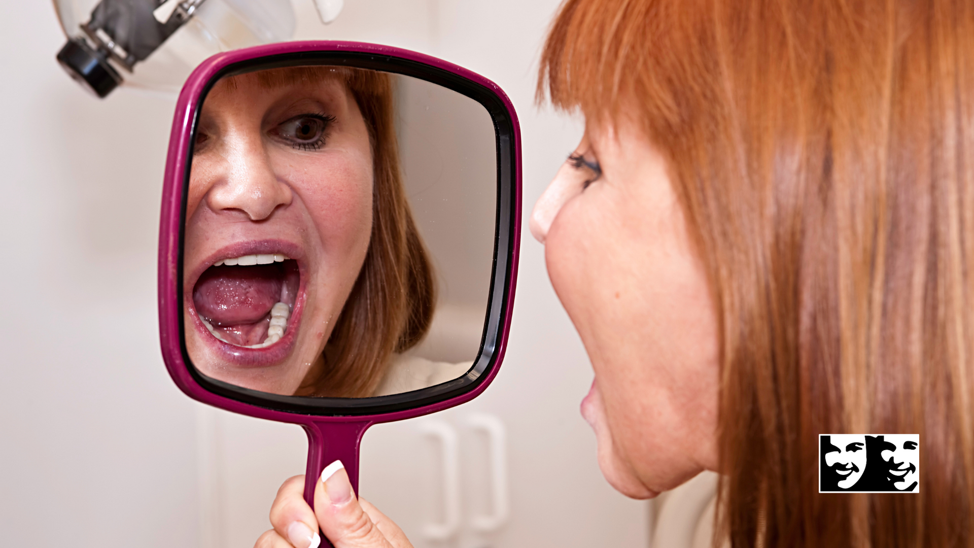 A woman is looking at her reflection in a hand mirror.