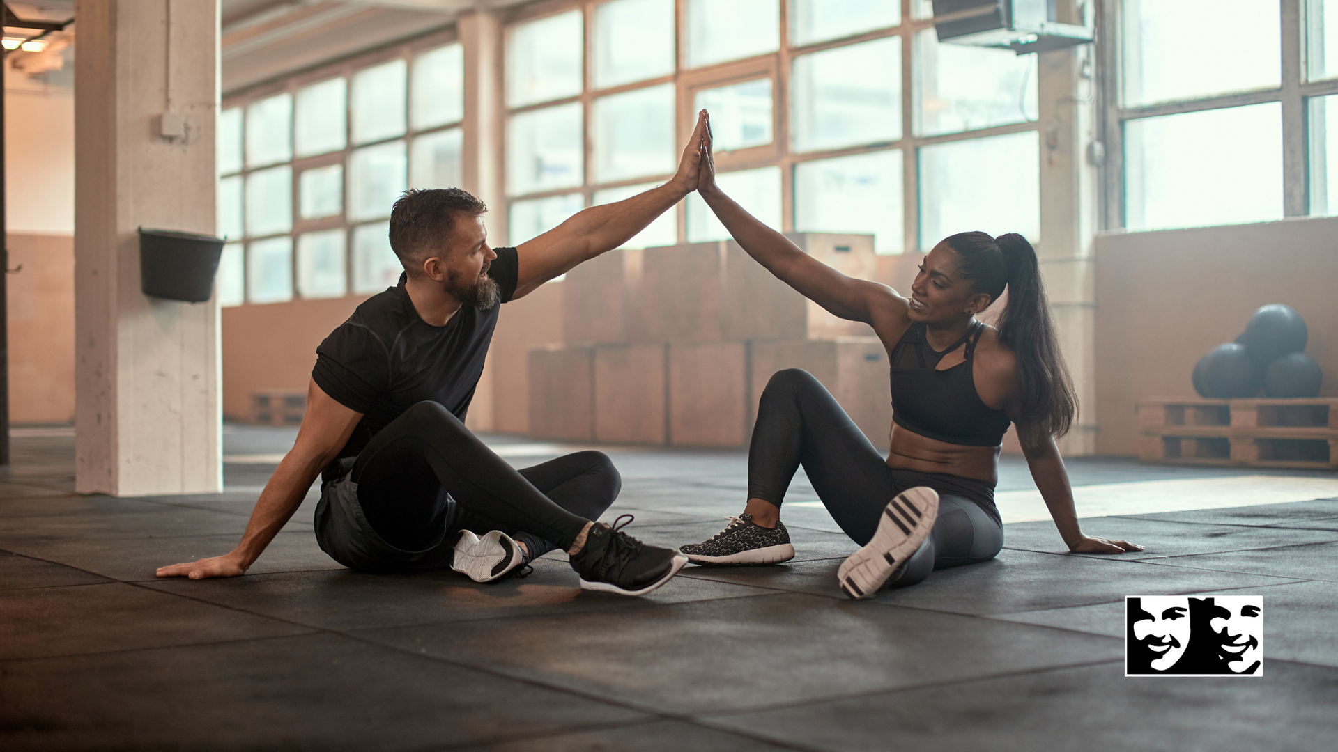 Man and woman in workout clothes give each other a high five in a gym.