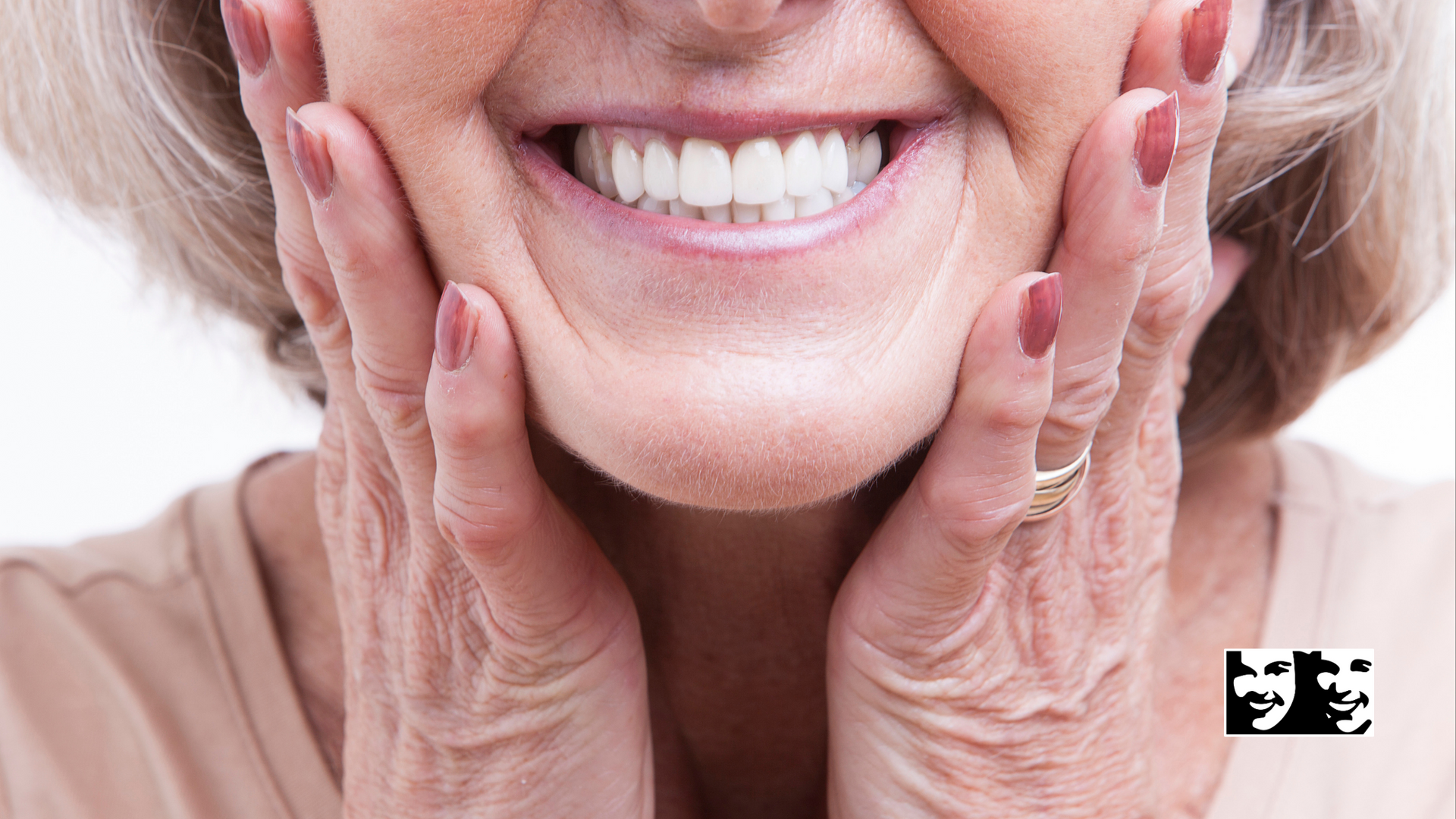 An elderly woman is smiling with her hands on her face.