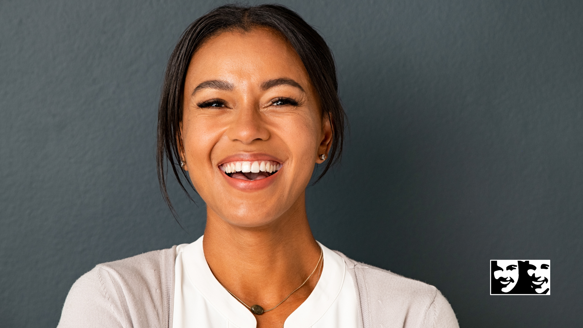 A woman is smiling in front of a gray wall.
