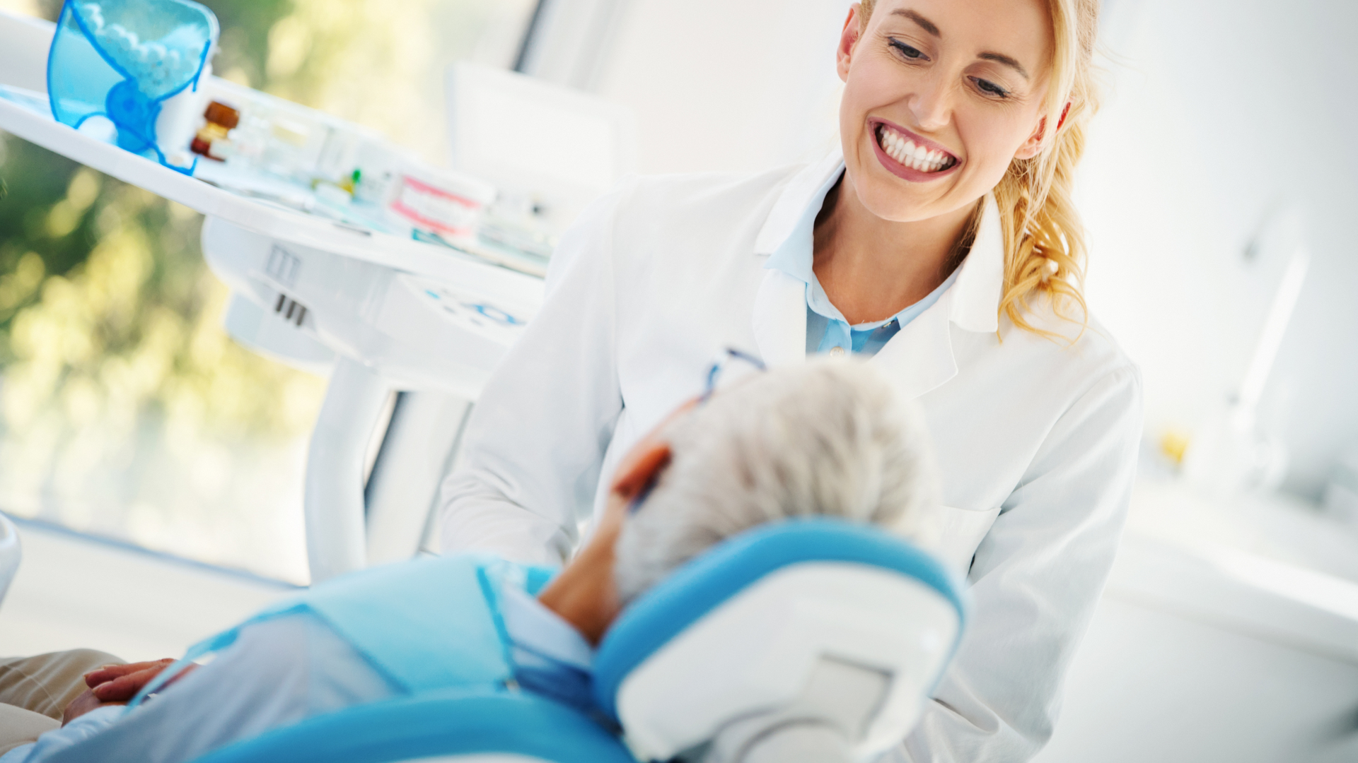 A dentist is smiling while talking to a patient in a dental chair.
