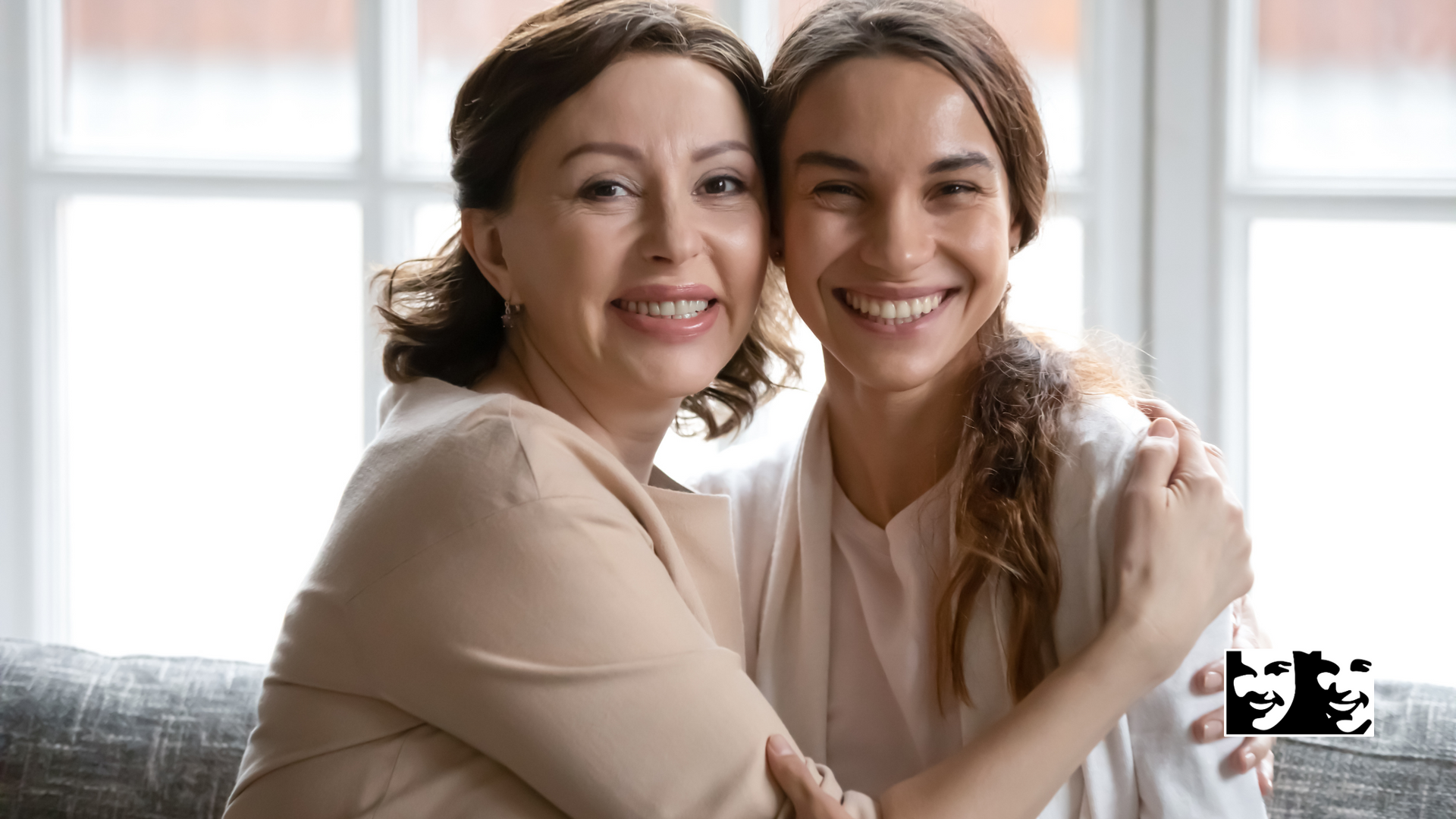 Two women are hugging each other and smiling while sitting on a couch.