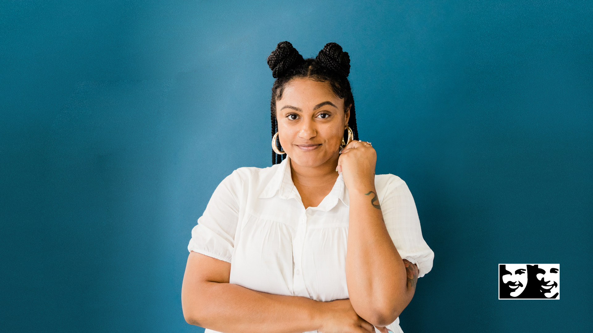 A woman in a white shirt is standing in front of a blue wall.