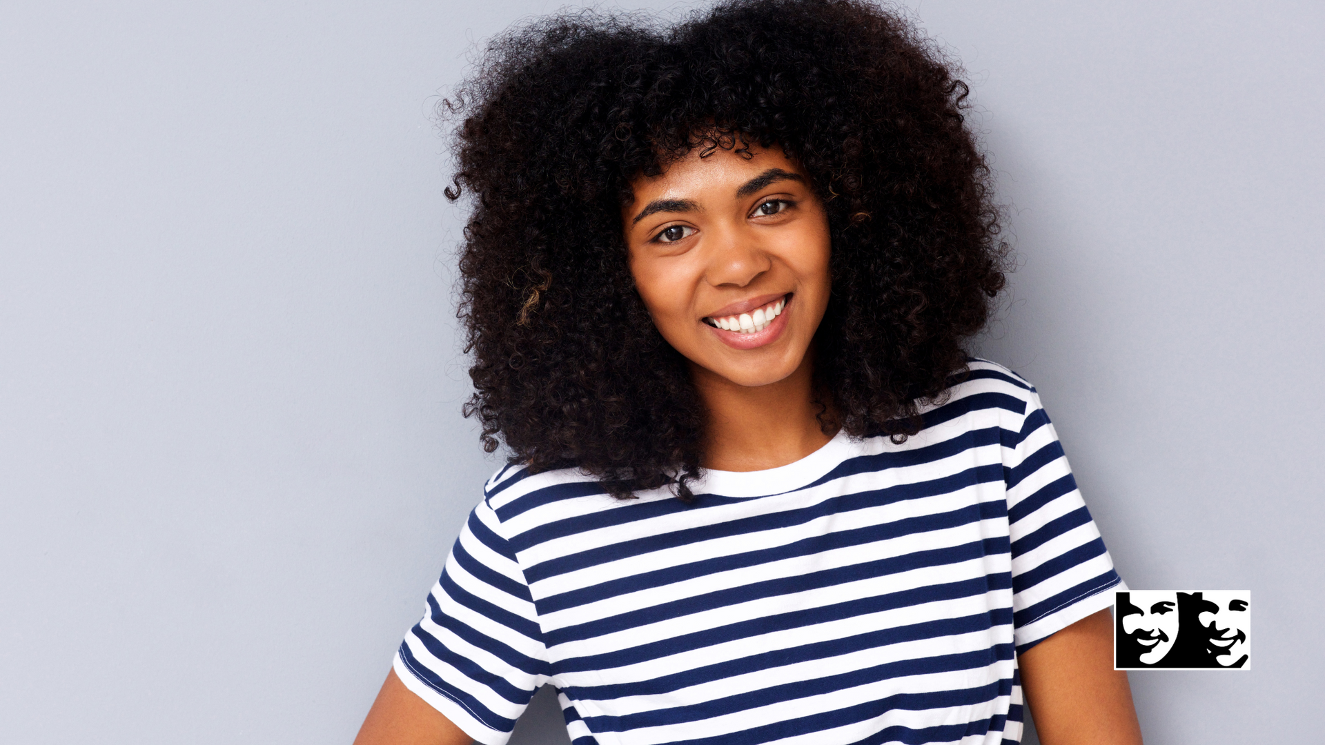 A woman with curly hair is wearing a striped shirt and smiling.