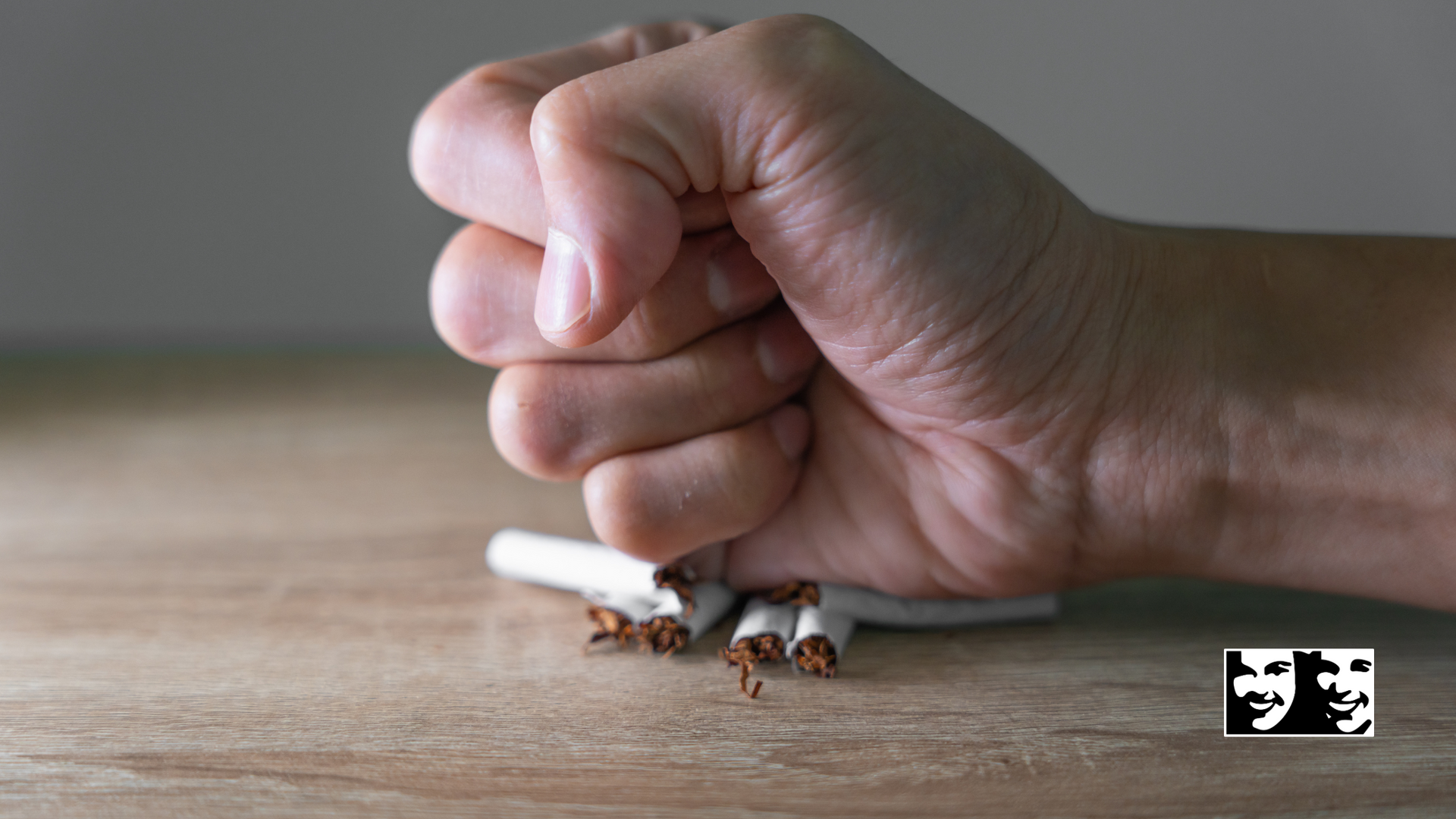 Hand crushing cigarettes on a wooden table; representing quitting smoking.