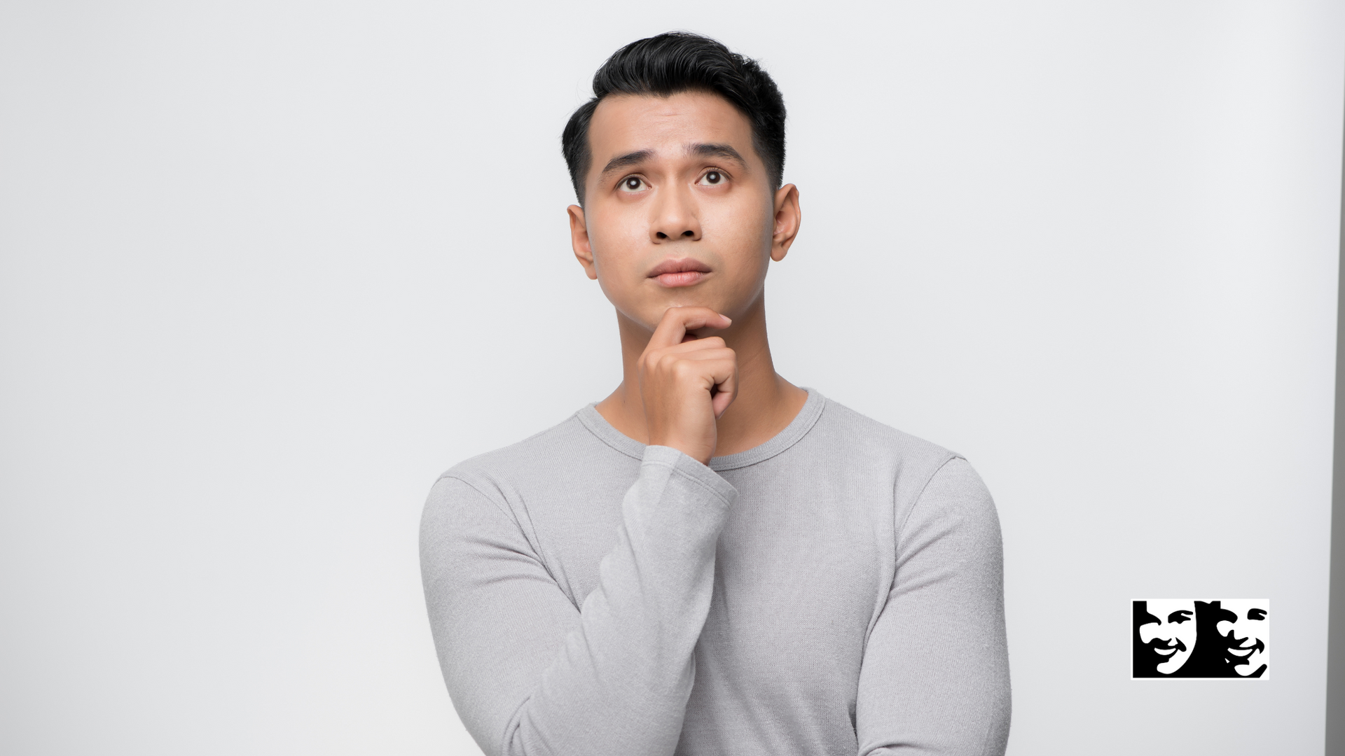 A man in a grey sweater is thinking with his hand on his chin.
