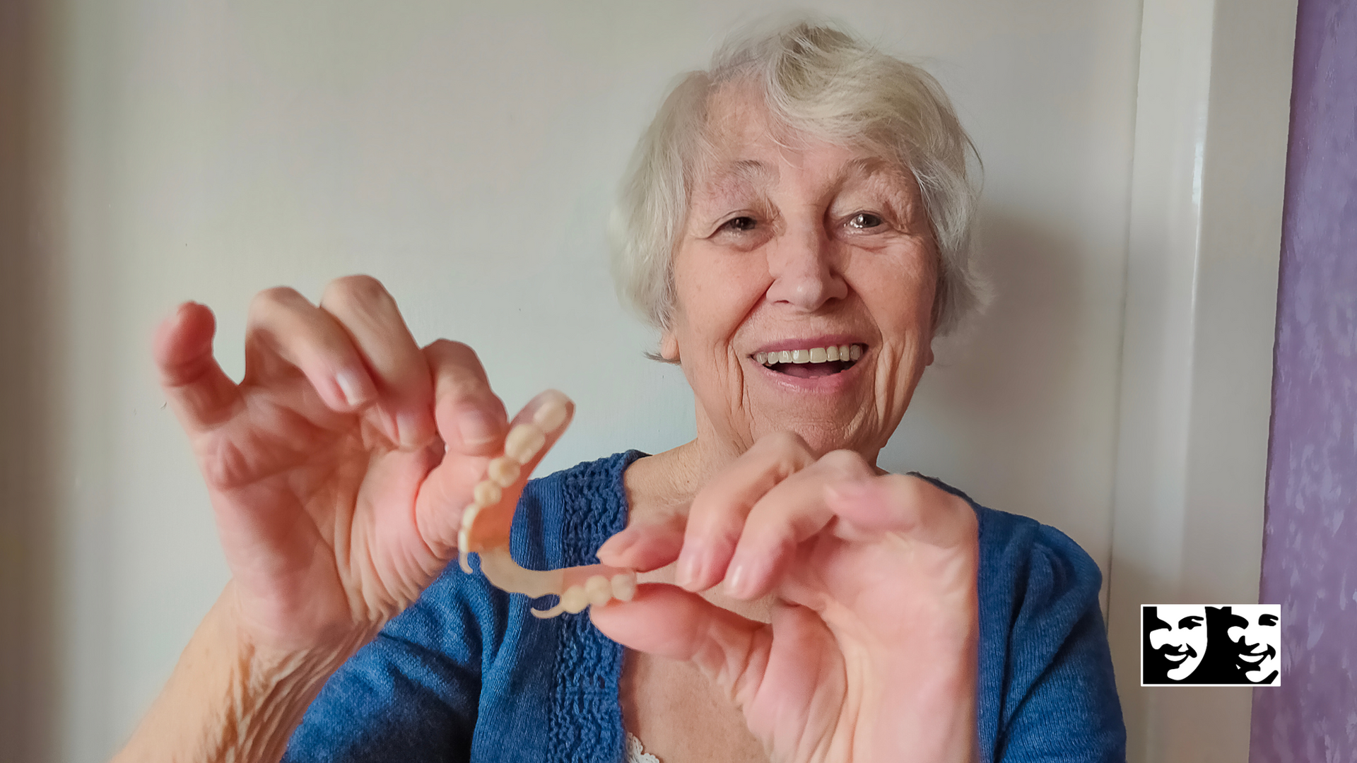 An elderly woman is holding a pair of dentures in her hands.