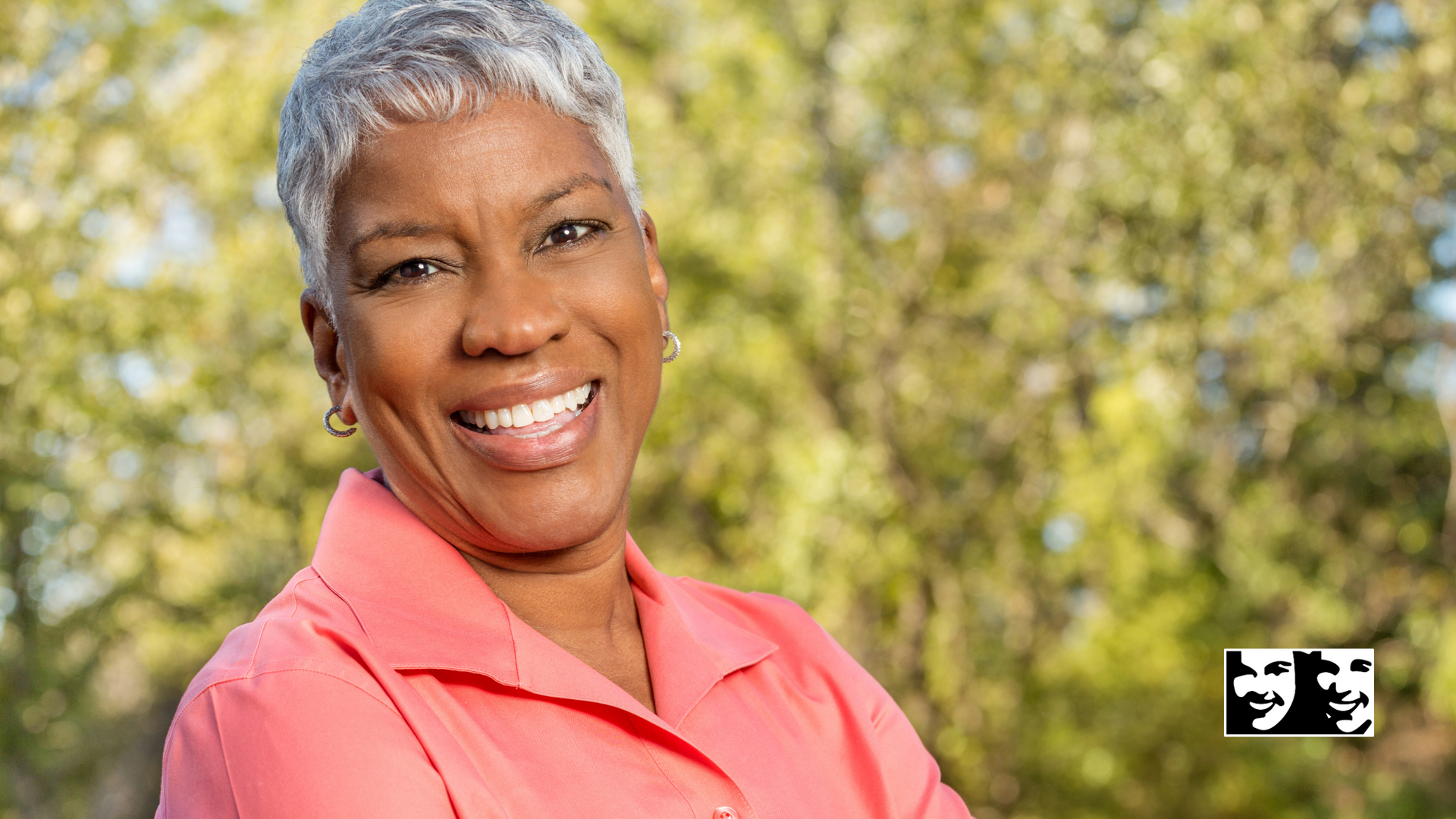 An older woman with gray hair is smiling with her arms crossed.