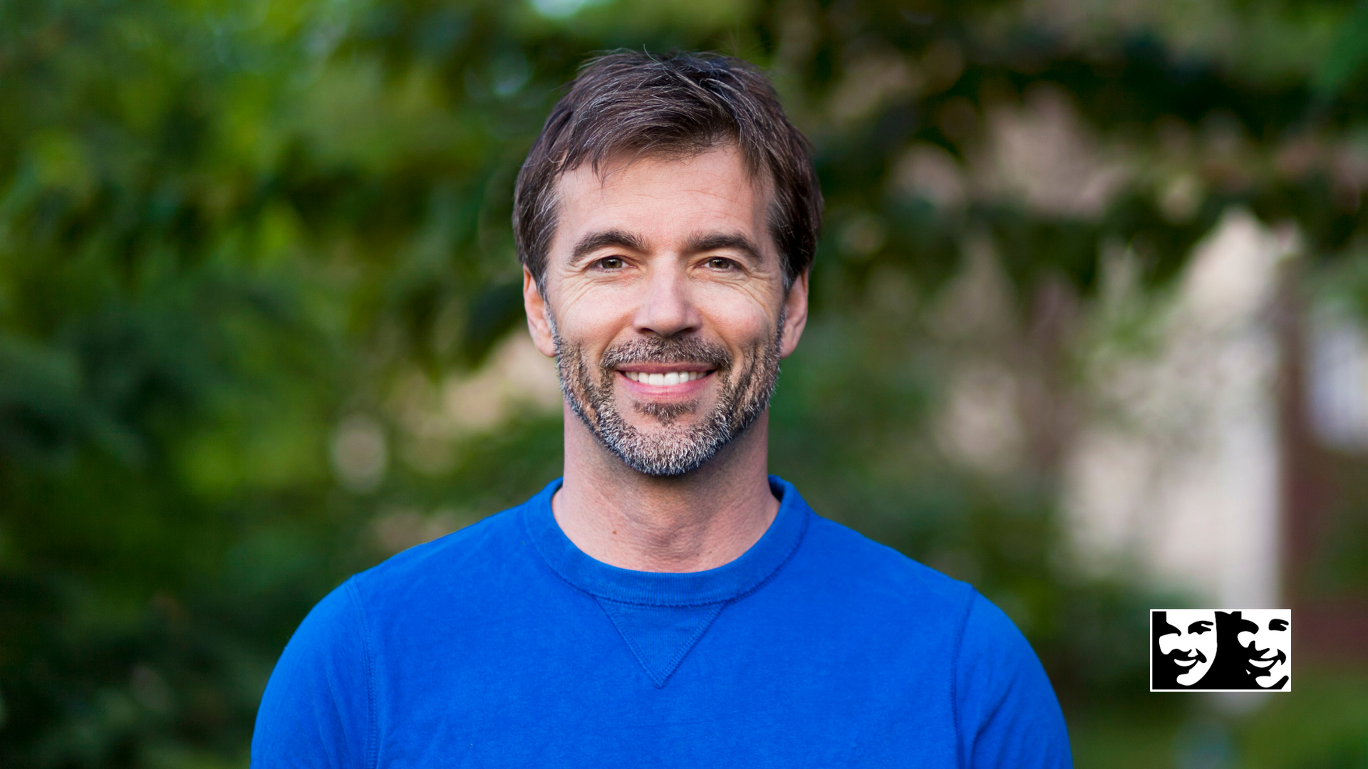 A man with a beard is wearing a blue shirt and smiling for the camera.