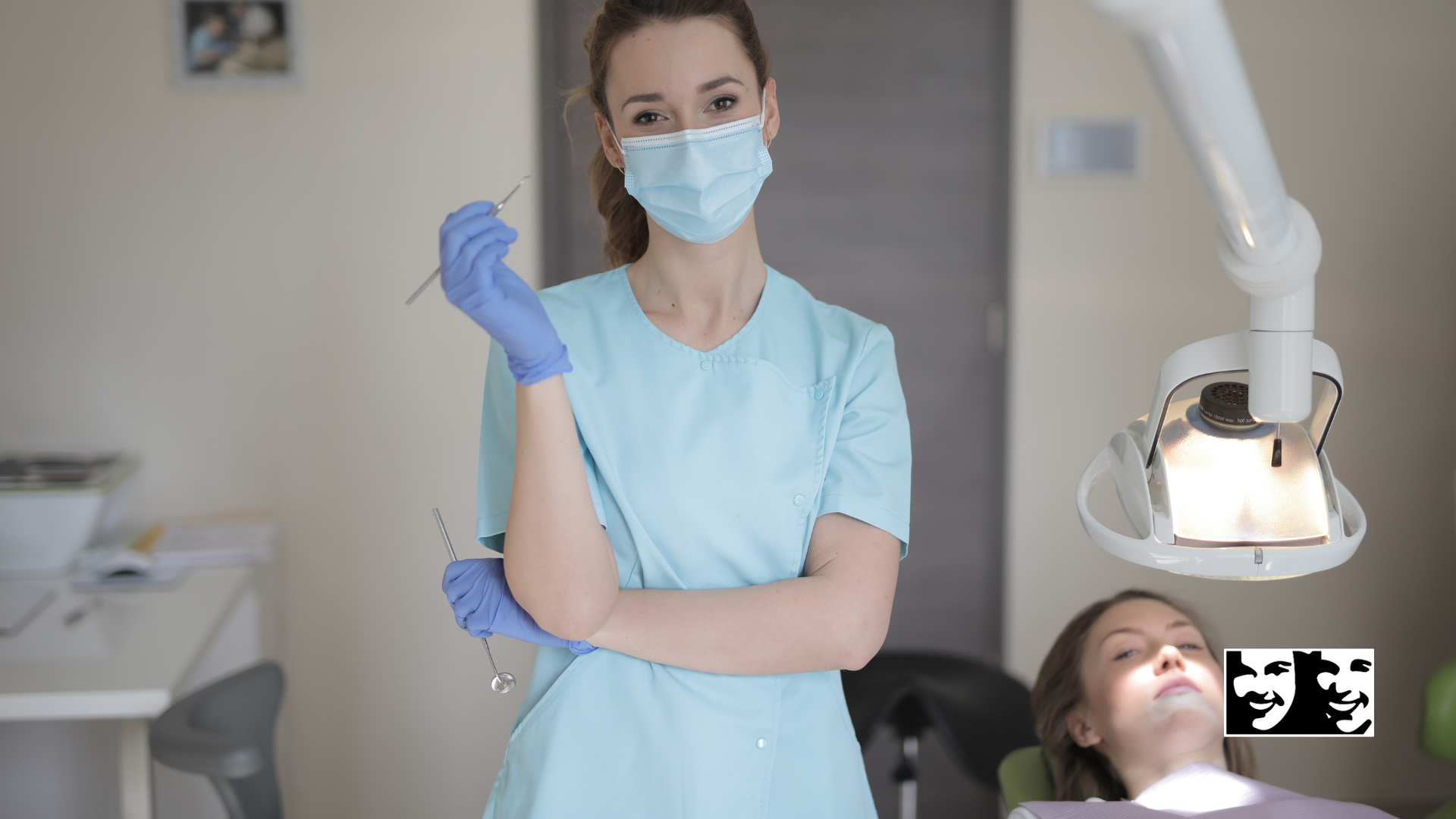A female dentist wearing a mask and gloves is standing next to a patient in a dental chair.