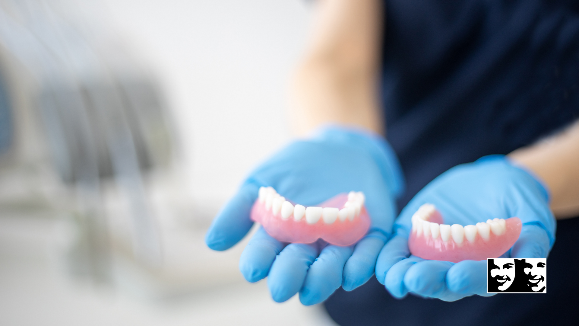 A person wearing blue gloves is holding two dentures in their hands.