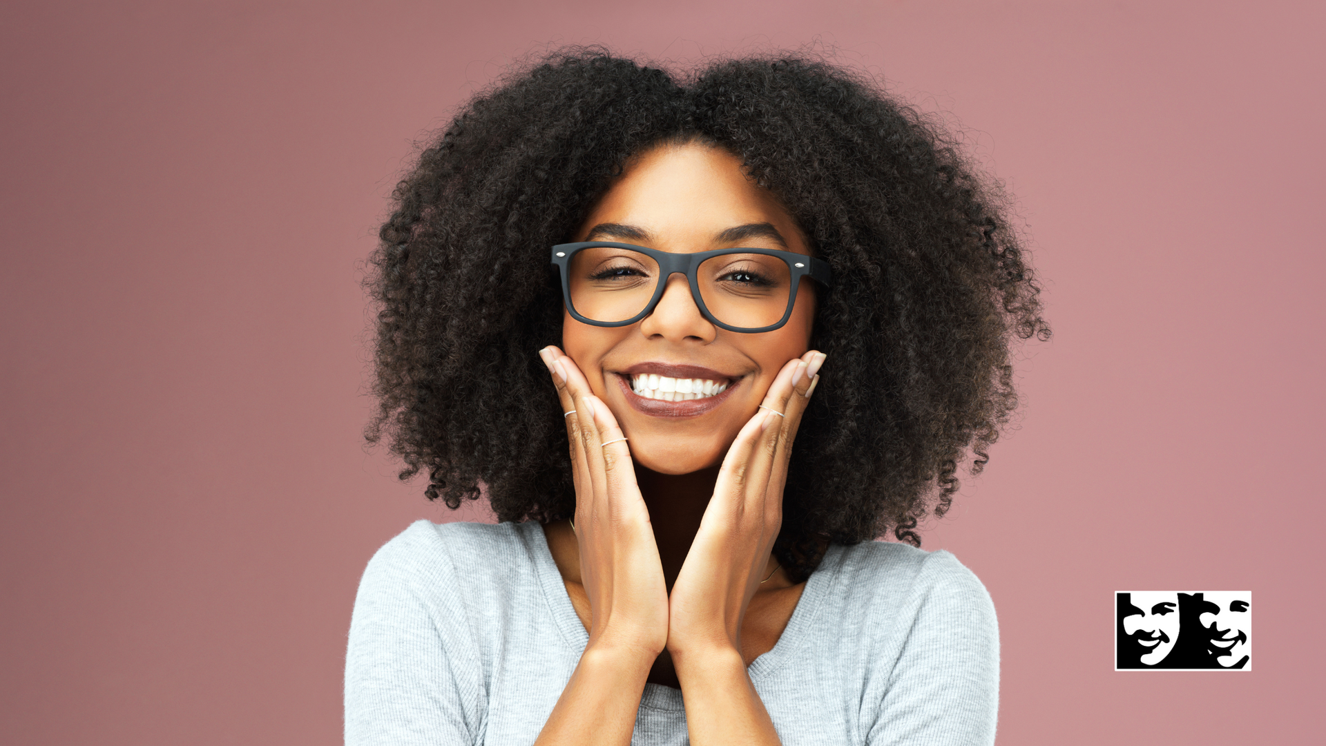 A woman wearing glasses is smiling and touching her face.