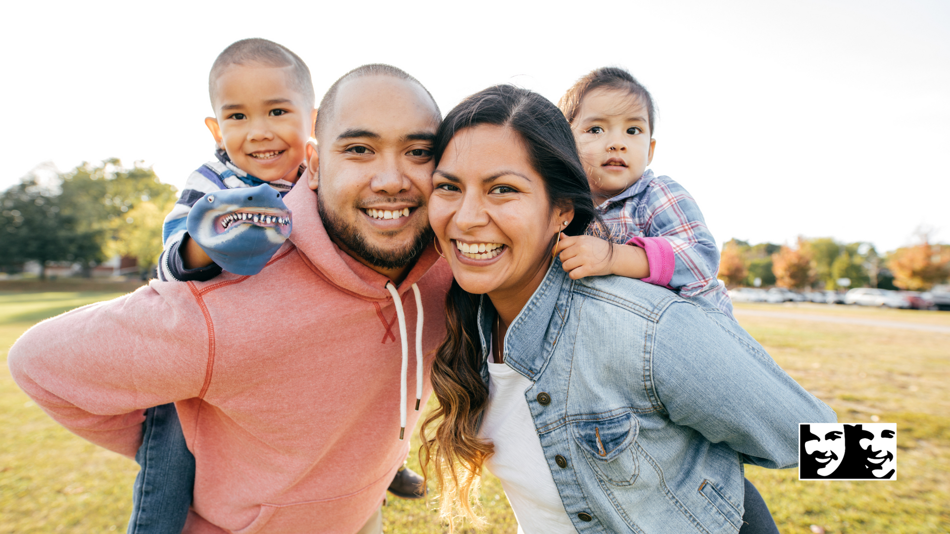 A man and woman are carrying two children on their shoulders in a park.