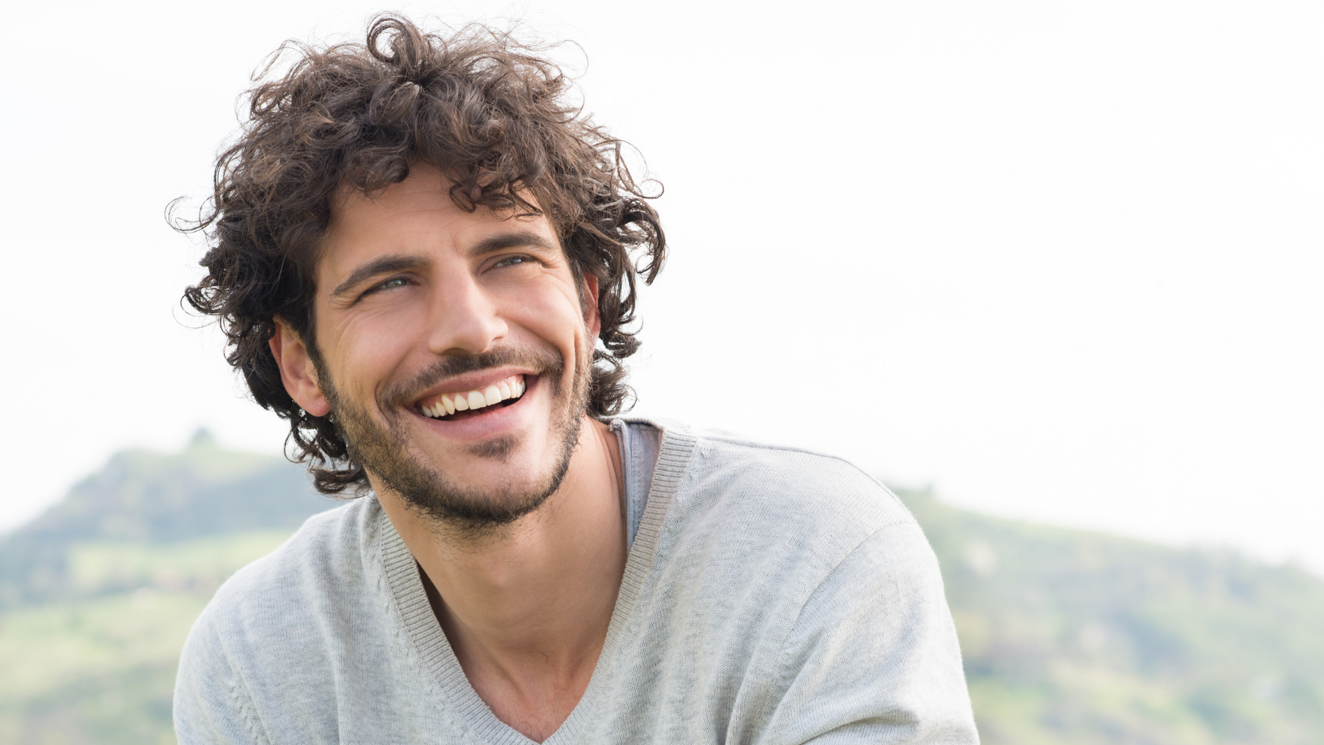A man with curly hair and a beard is smiling.