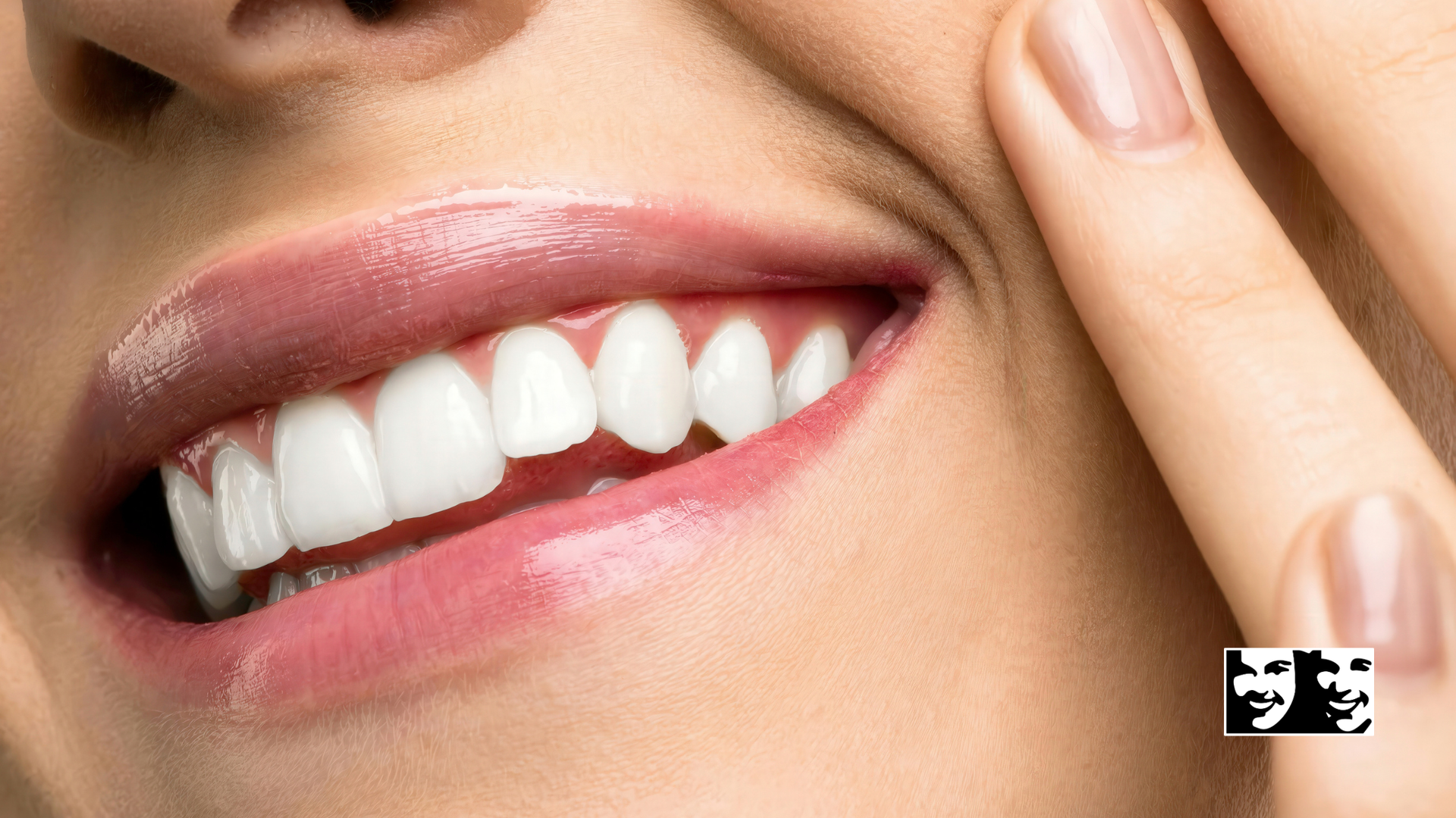 Close-up of a smiling mouth with bright white teeth and glossy pink lips, person touching cheek.